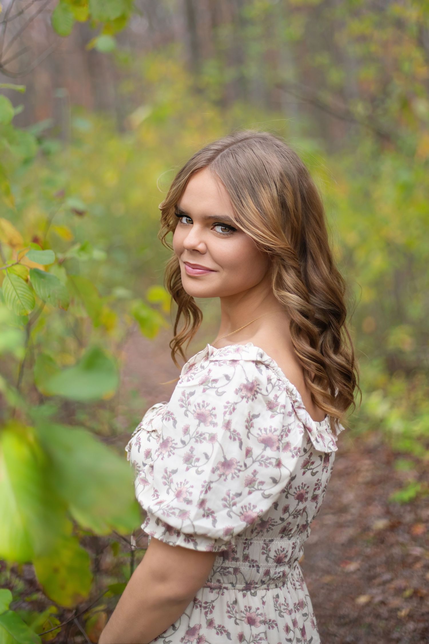 Portrait in floral dress with soft lighting and natural woodland background.