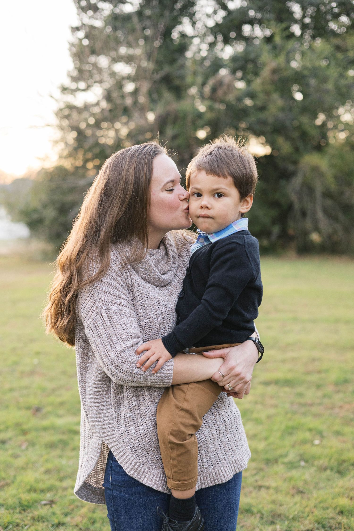 A tender moment between parent and child in a grassy field wearing cozy sweaters at sunset.