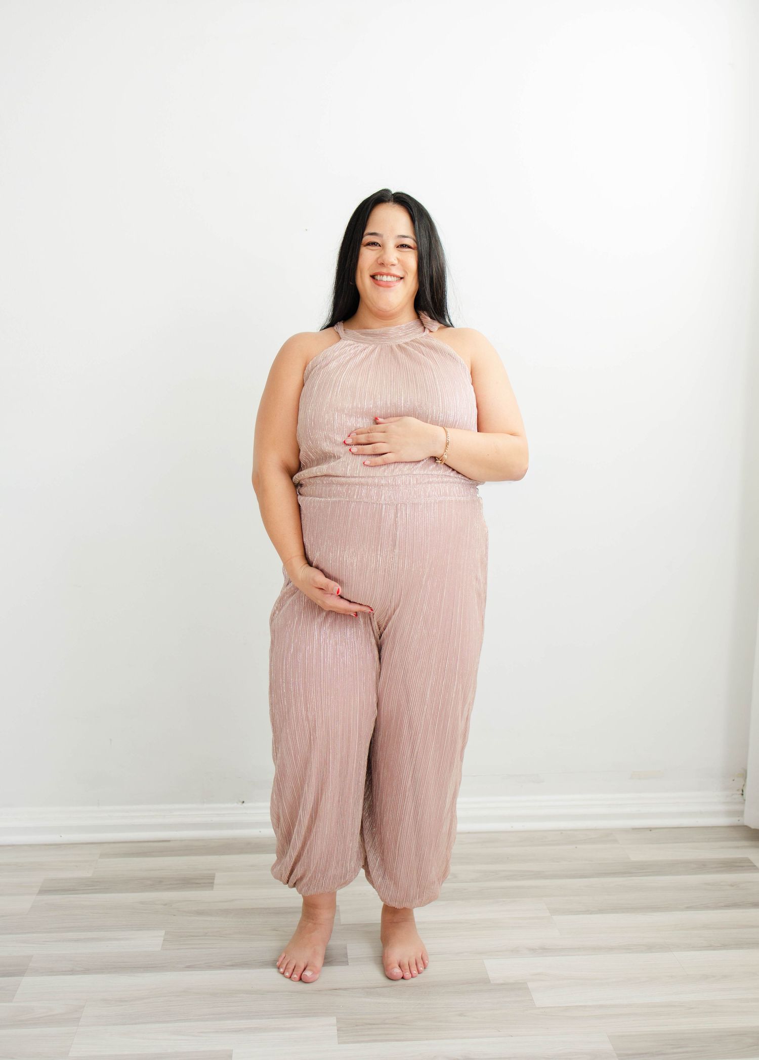 Pregnant woman in blush-colored outfit smiles during studio maternity photography session.