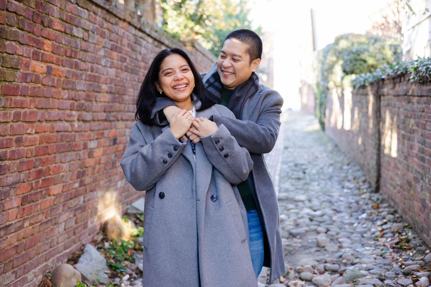Romantic couple sharing tender moments against a brick wall backdrop in matching winter coats.