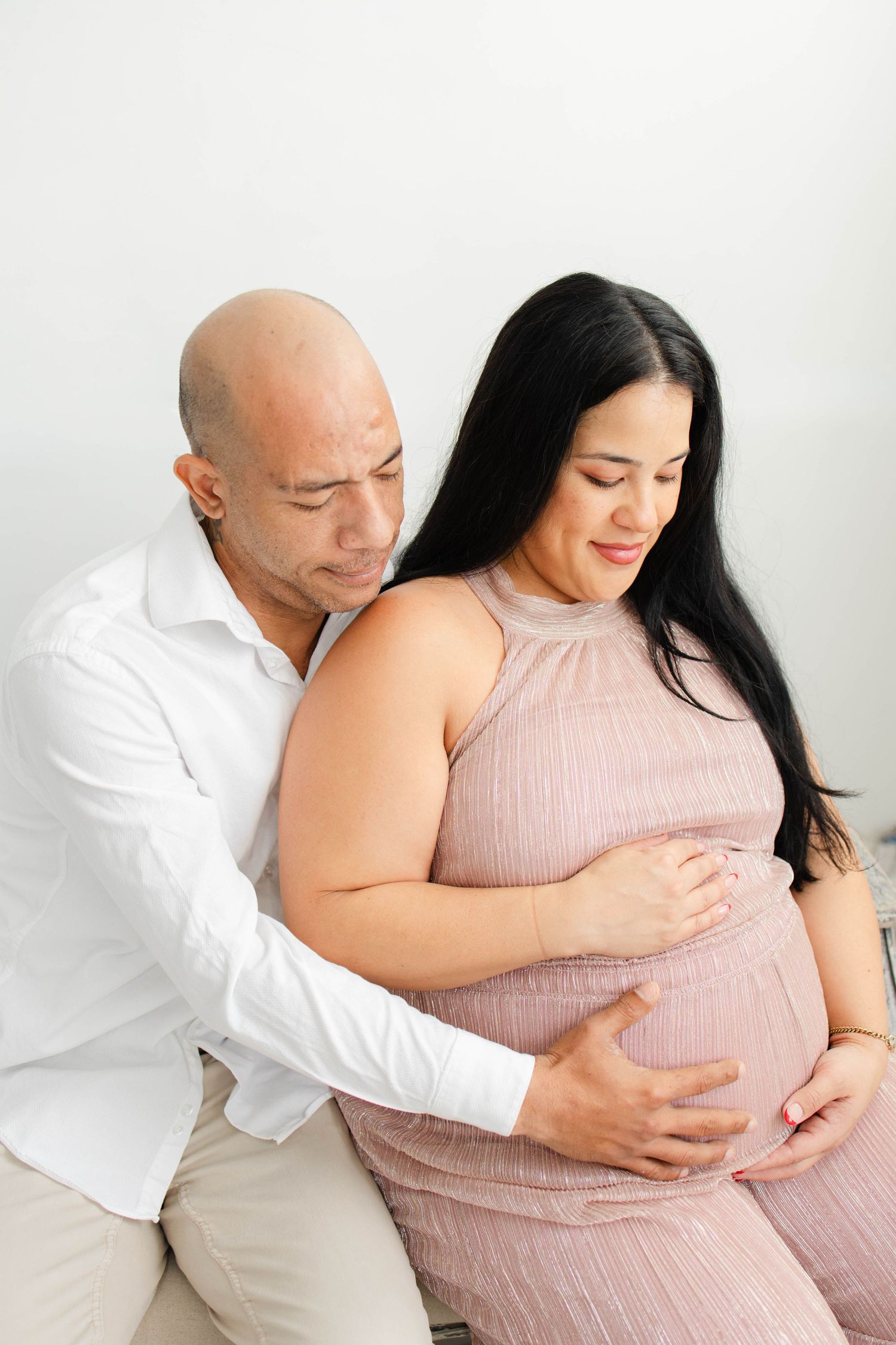 Expectant couple poses for romantic maternity photos in minimalist white studio.