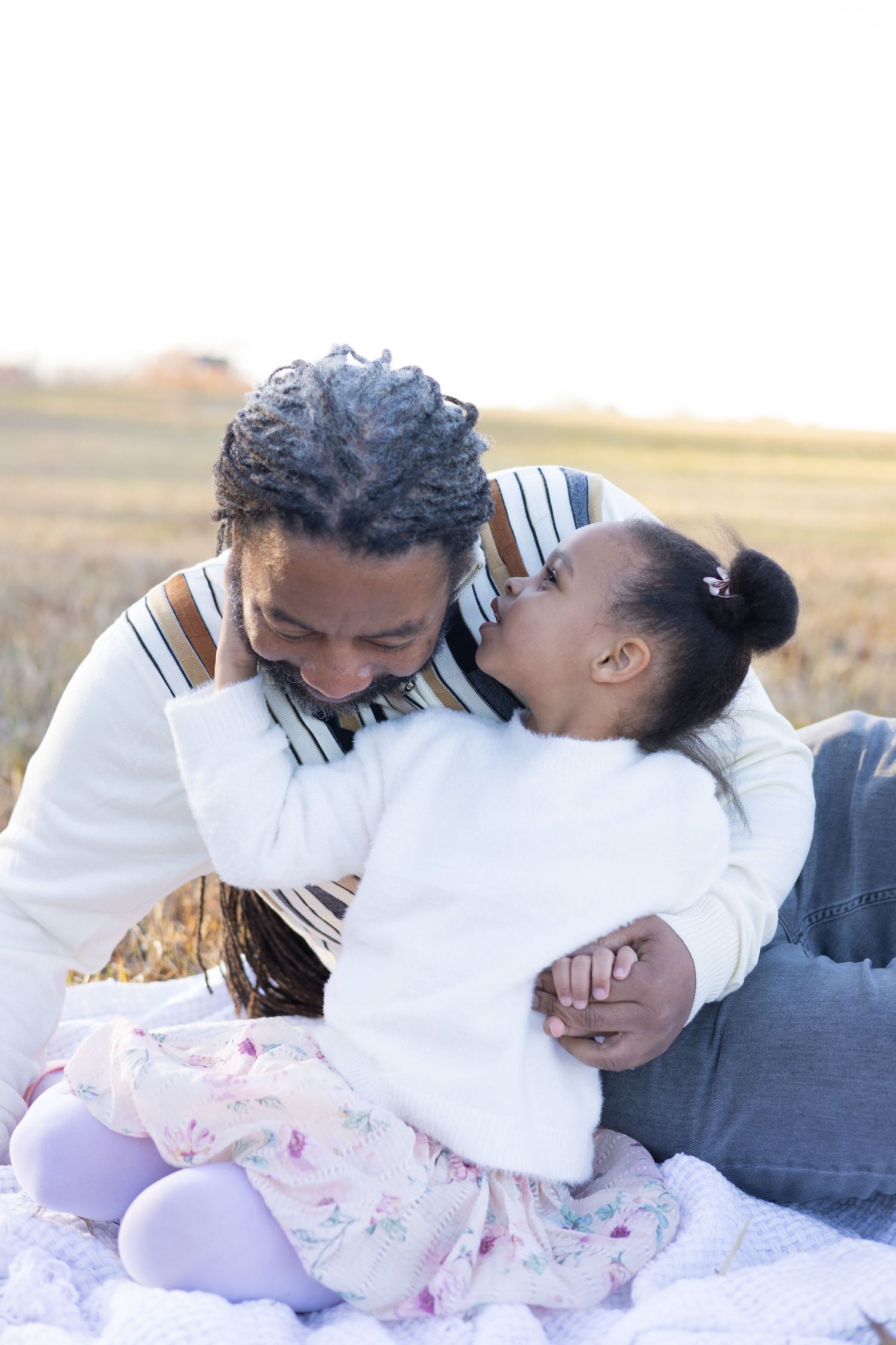 Playful outdoor family photoshoot with white sweaters and jeans in a golden field at sunset.