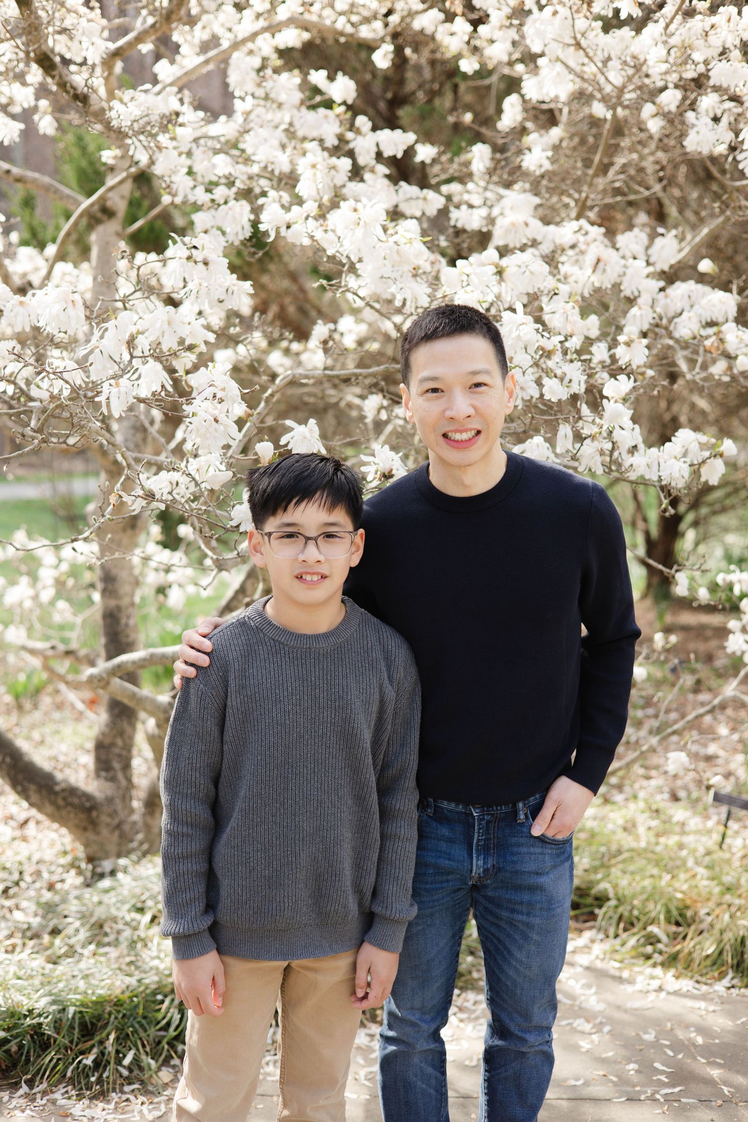 A man and boy pose together in front of a blooming white magnolia tree in spring.