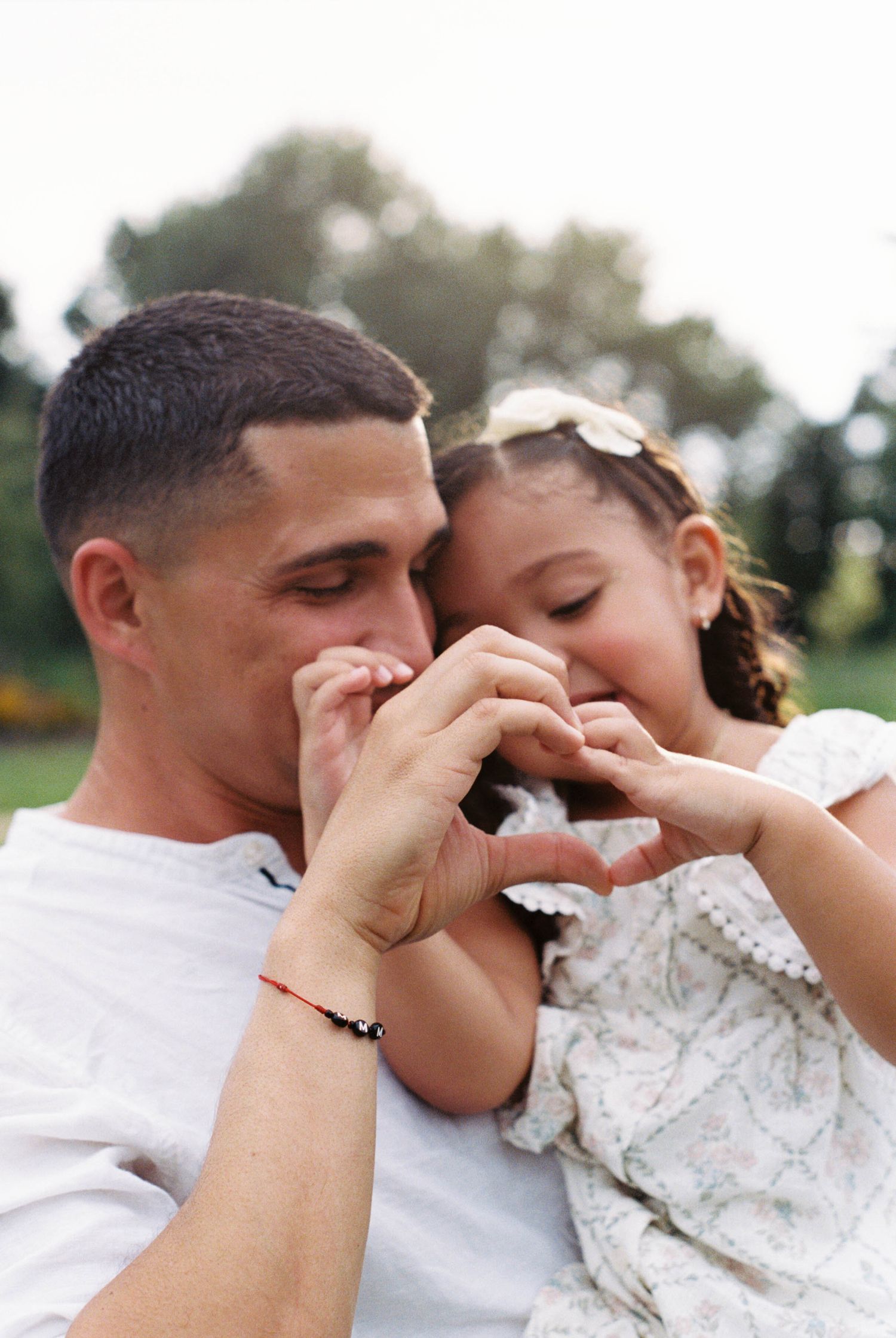 Father and daughter making a heart shape with their hands together in a park, sharing a tender moment.