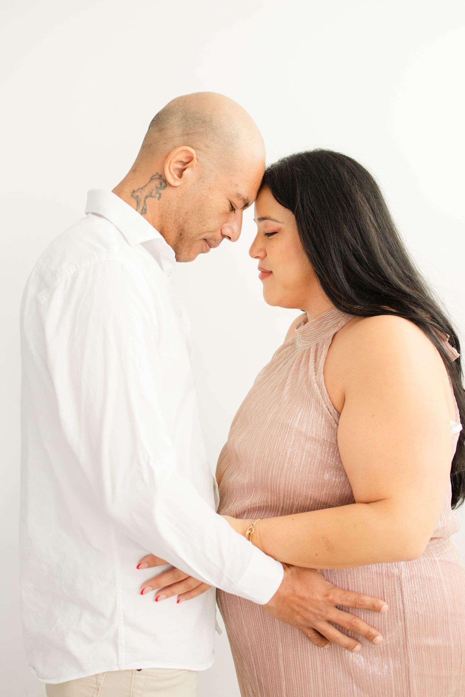 Intimate maternity portraits capture tender moments between couple against white backdrop.