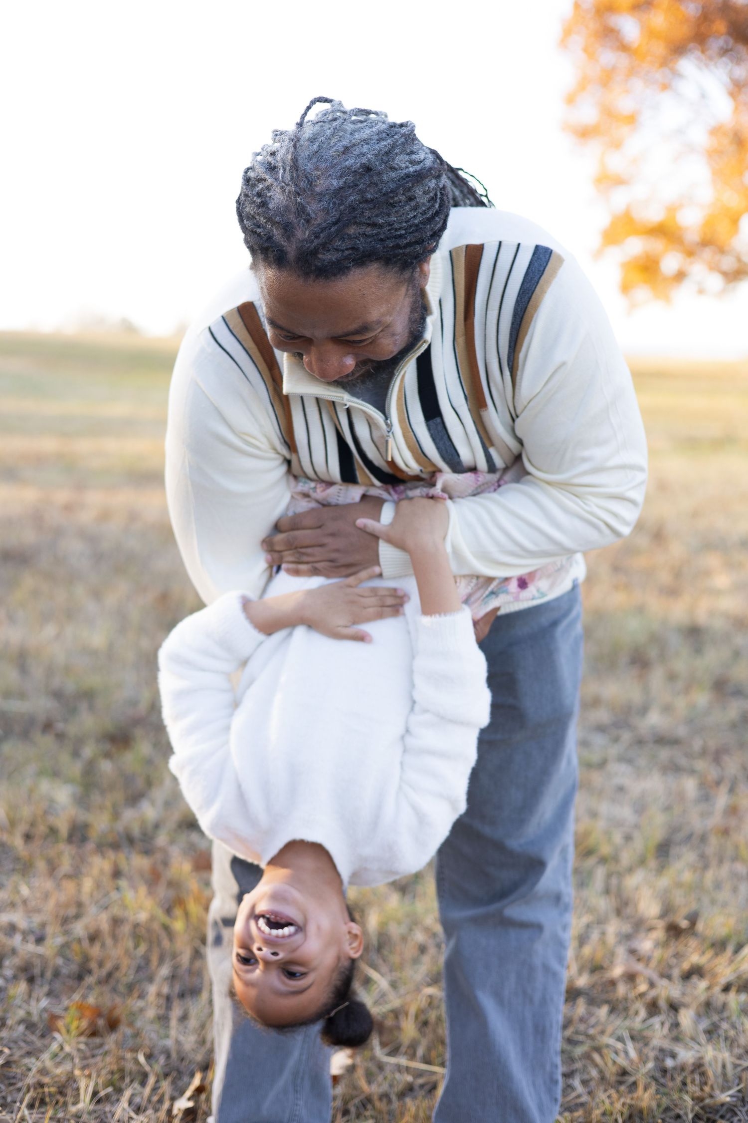 Playful upside-down moment between family members in white sweaters.
