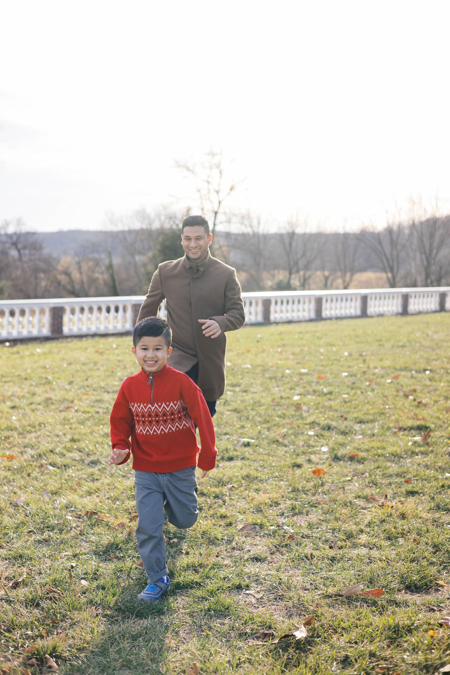 A child in a red sweater runs playfully across a grassy field.