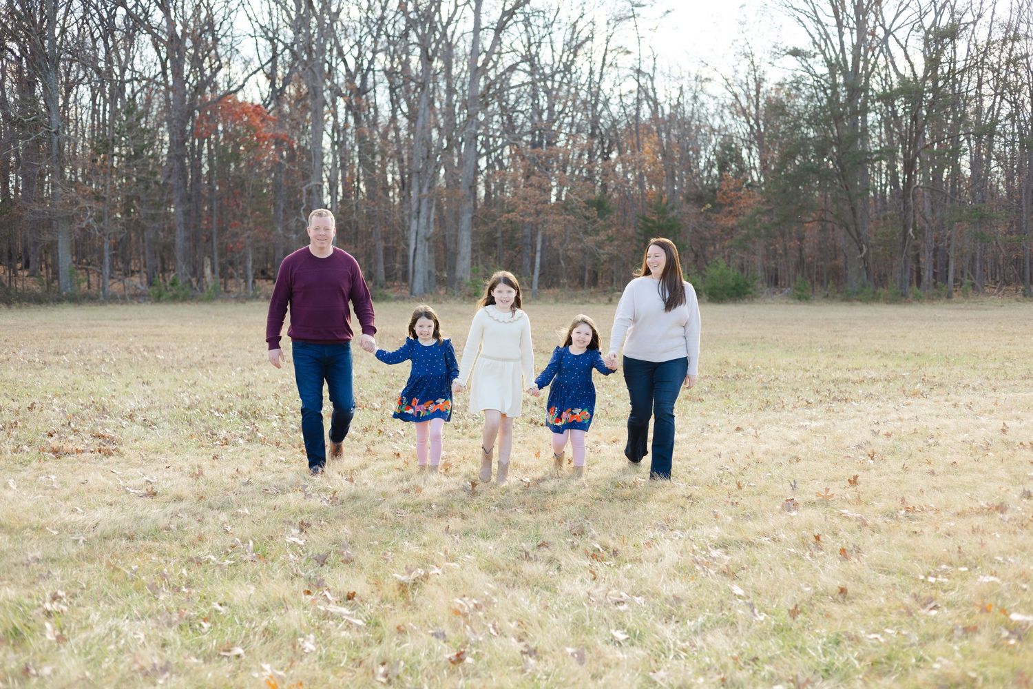 Family walking together through an autumn field with bare trees in the background.