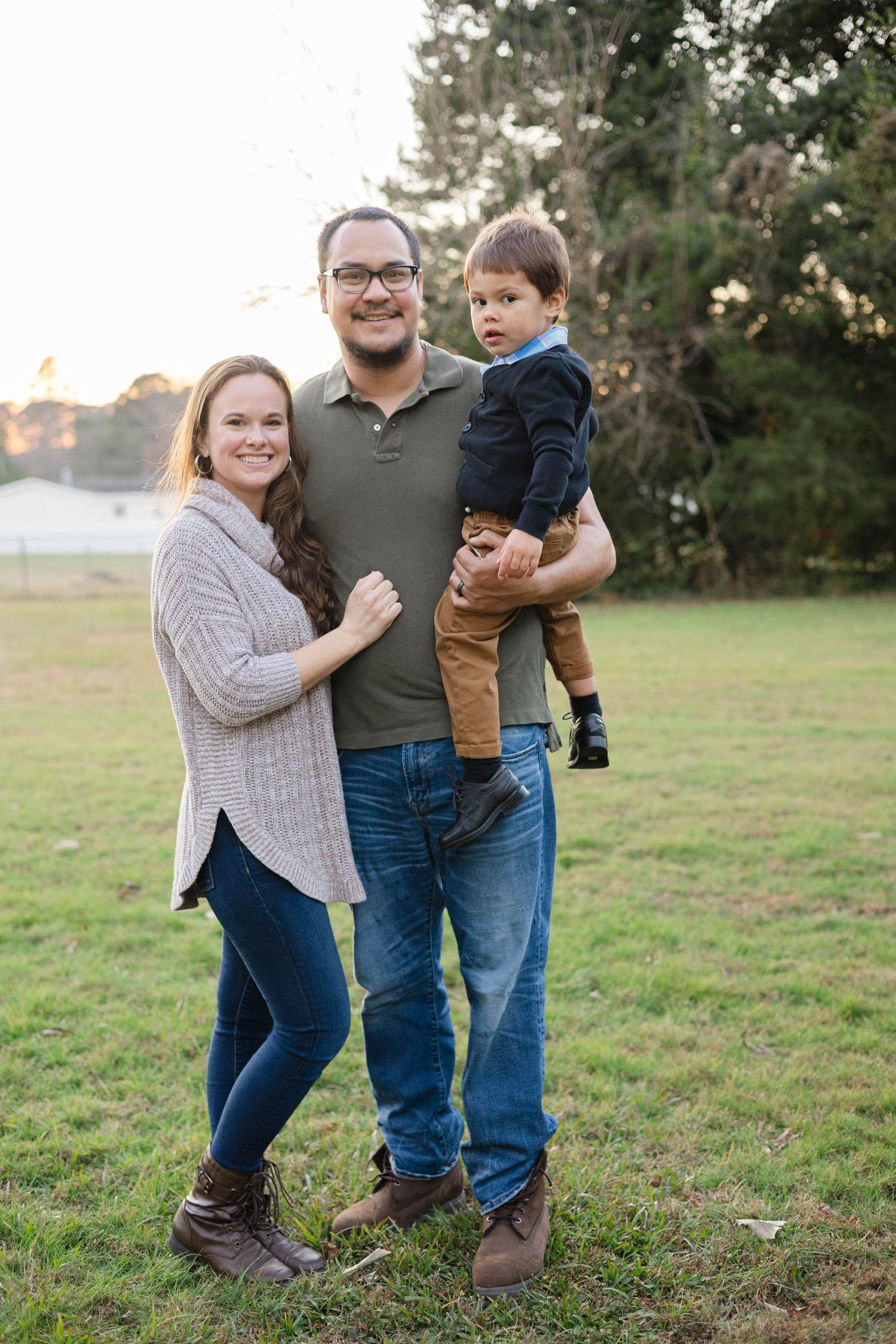 Family enjoying outdoor photo session in a grassy field at sunset wearing casual sweaters and jeans.