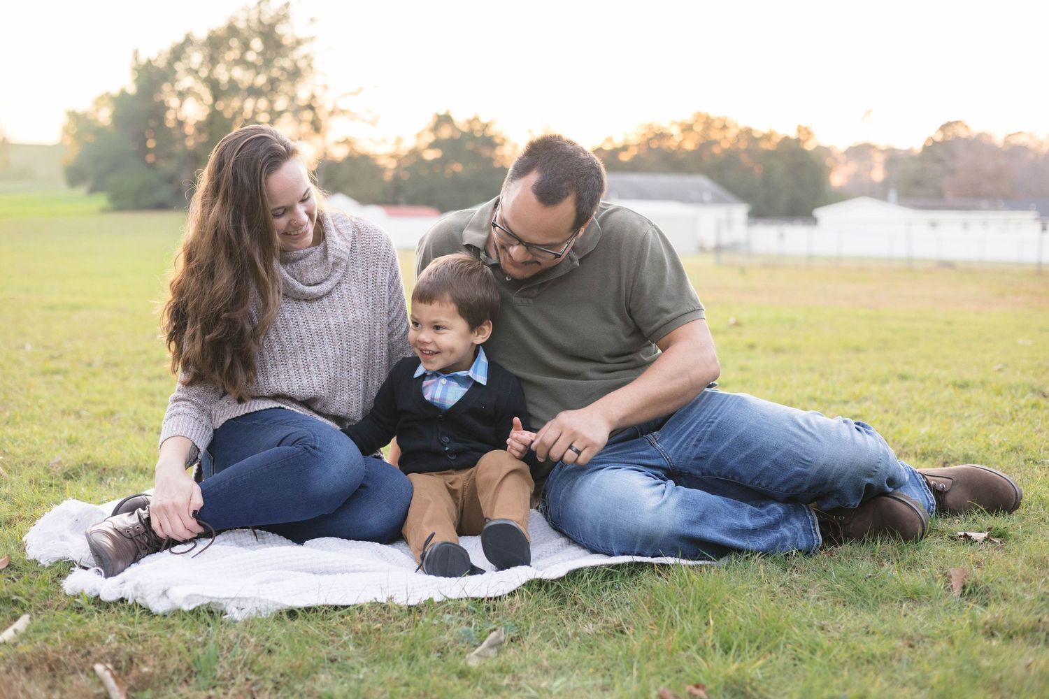 Family relaxing together on blanket in grassy field during golden hour photoshoot.
