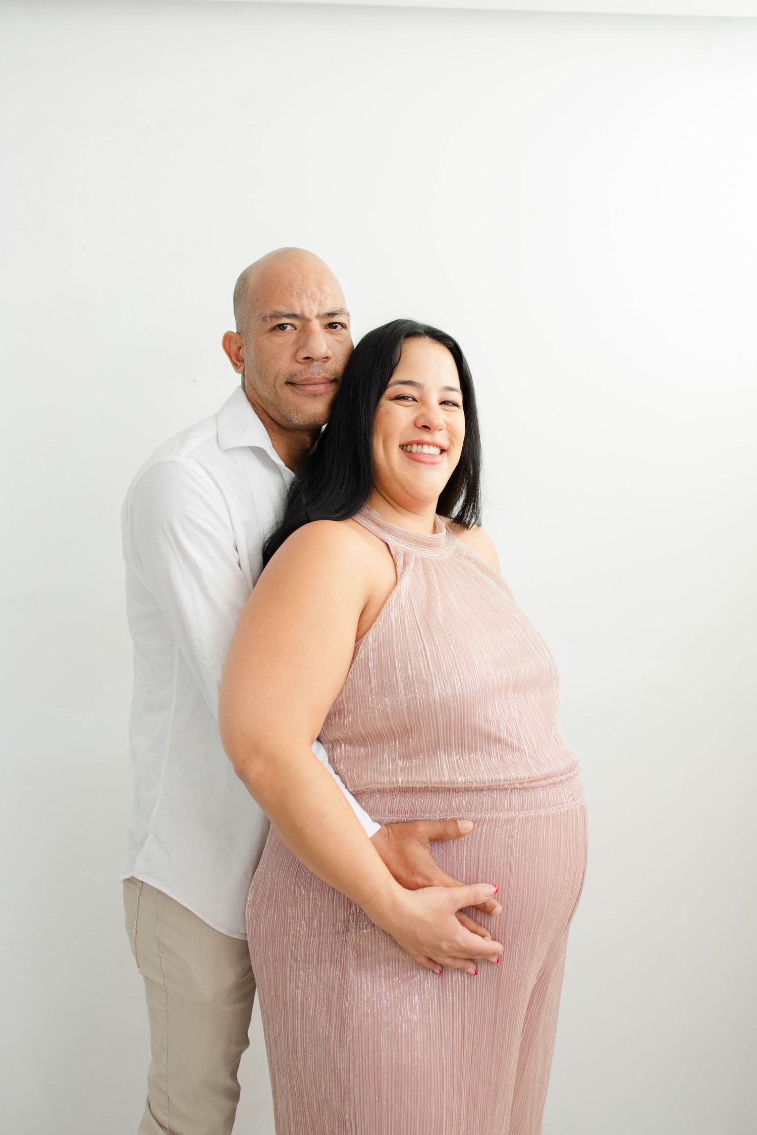 Joyful maternity photoshoot featuring couple in pink dress and white shirt.