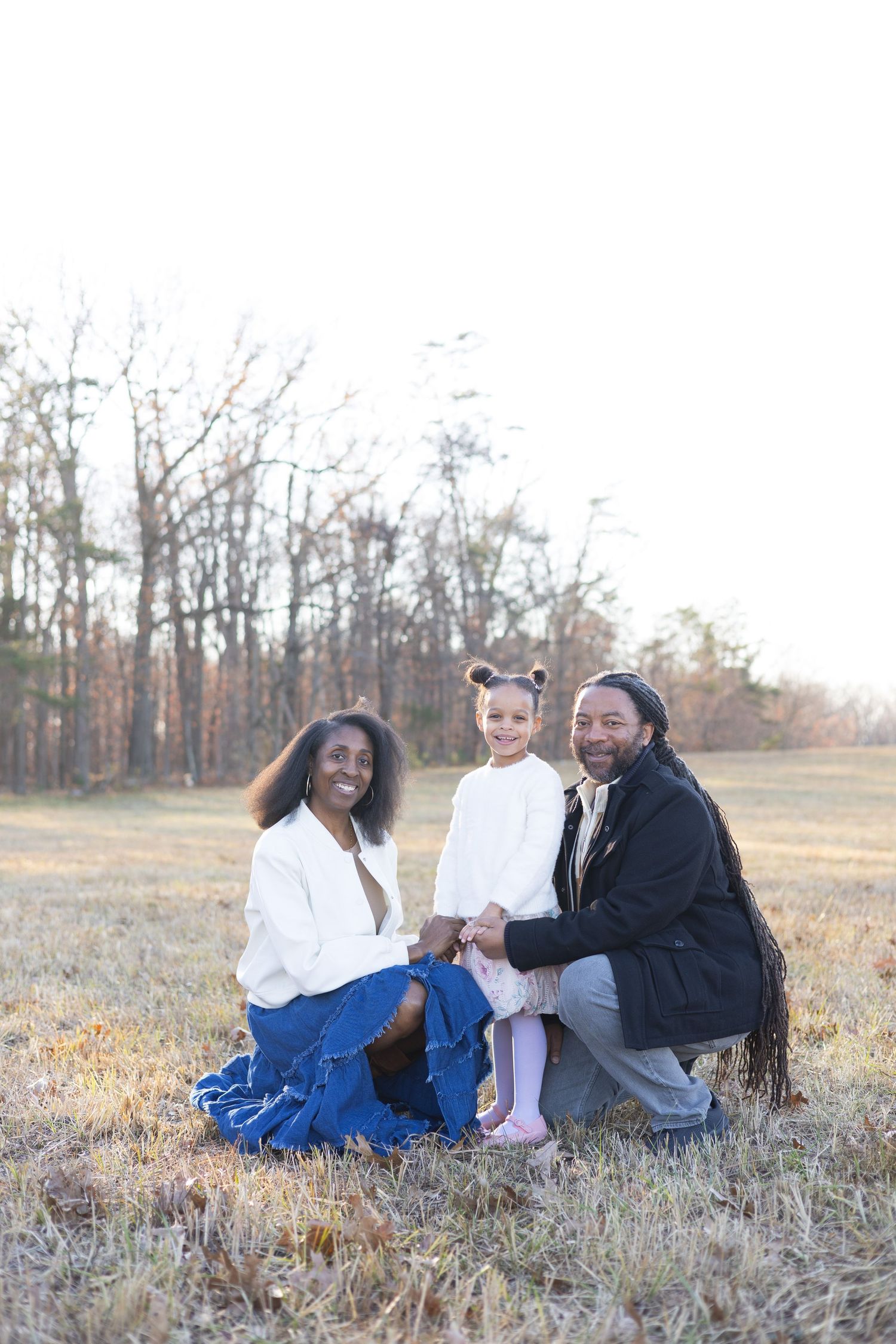 Family lounging together on dried grass in an autumn field during sunset.
