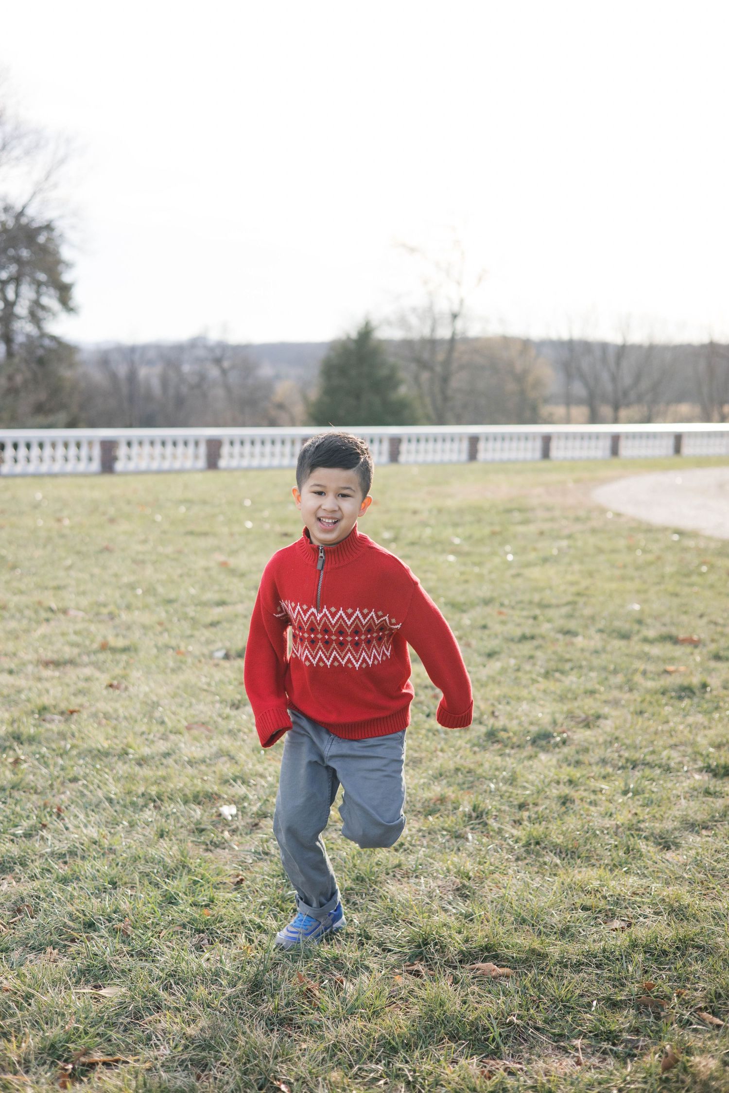 A child wearing a festive red sweater runs happily through a grassy field.