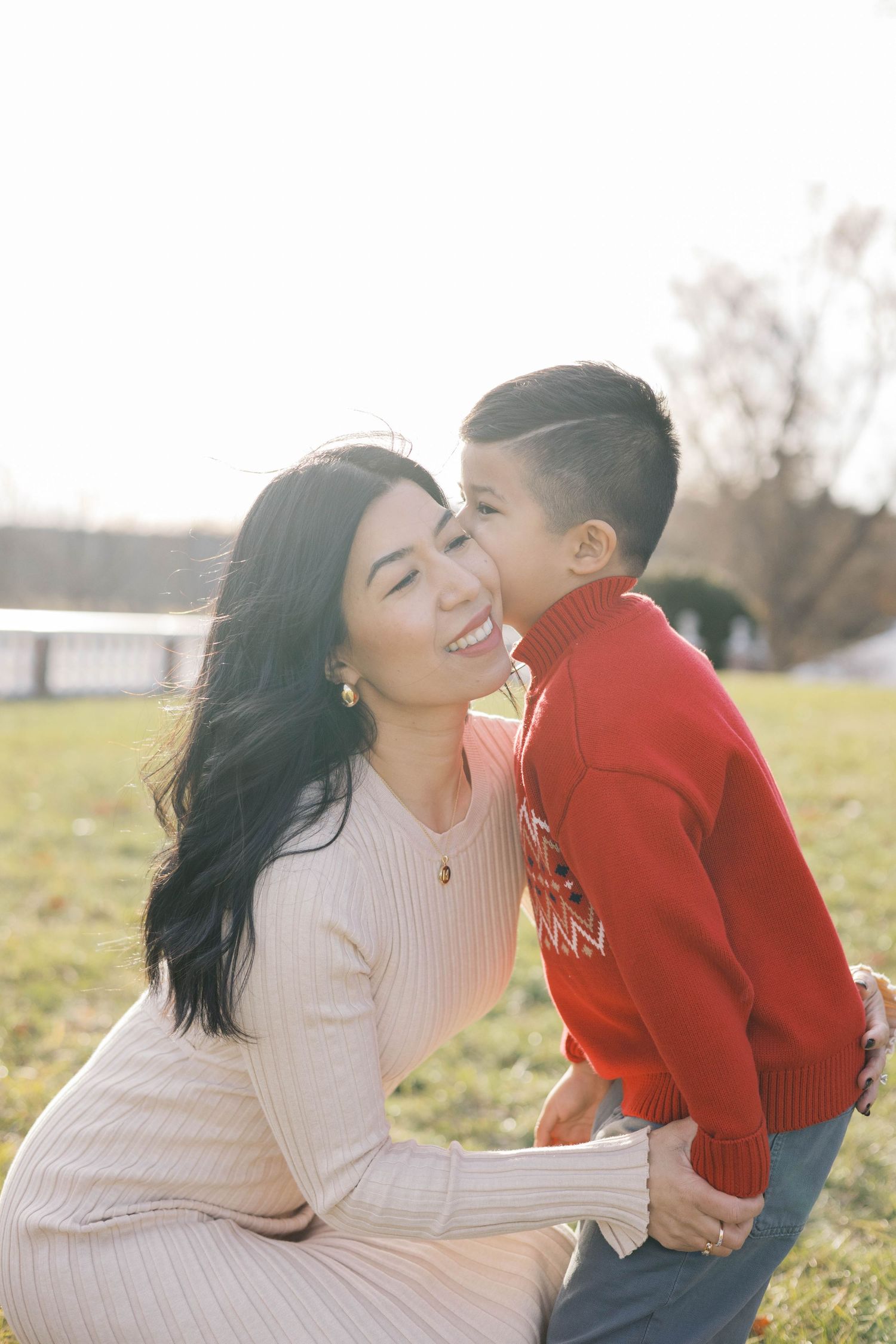 Tender family moments captured in a sunlit field with warm sweaters and genuine smiles.