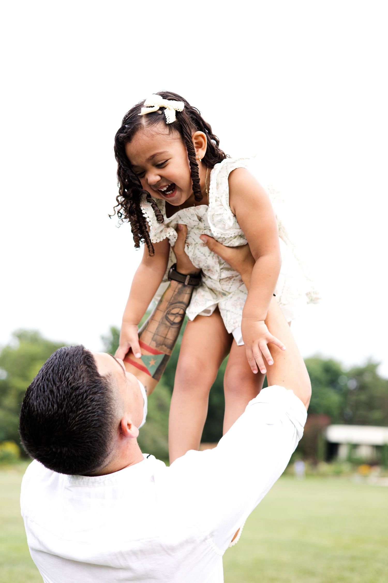 A joyful father lifts his laughing young daughter high in the air outdoors on a green lawn.