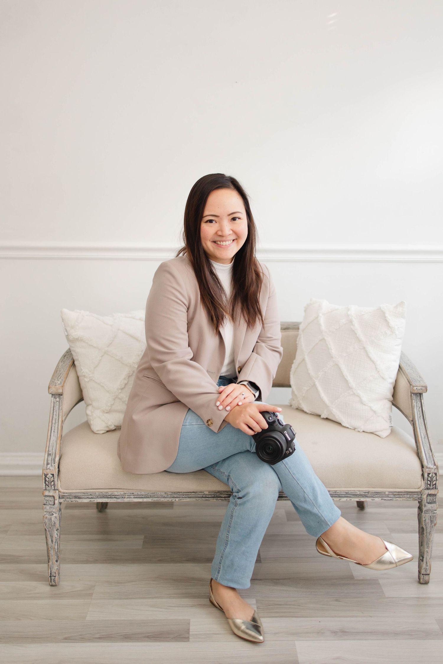 Professional photographer poses on elegant white bench in casual attire.
