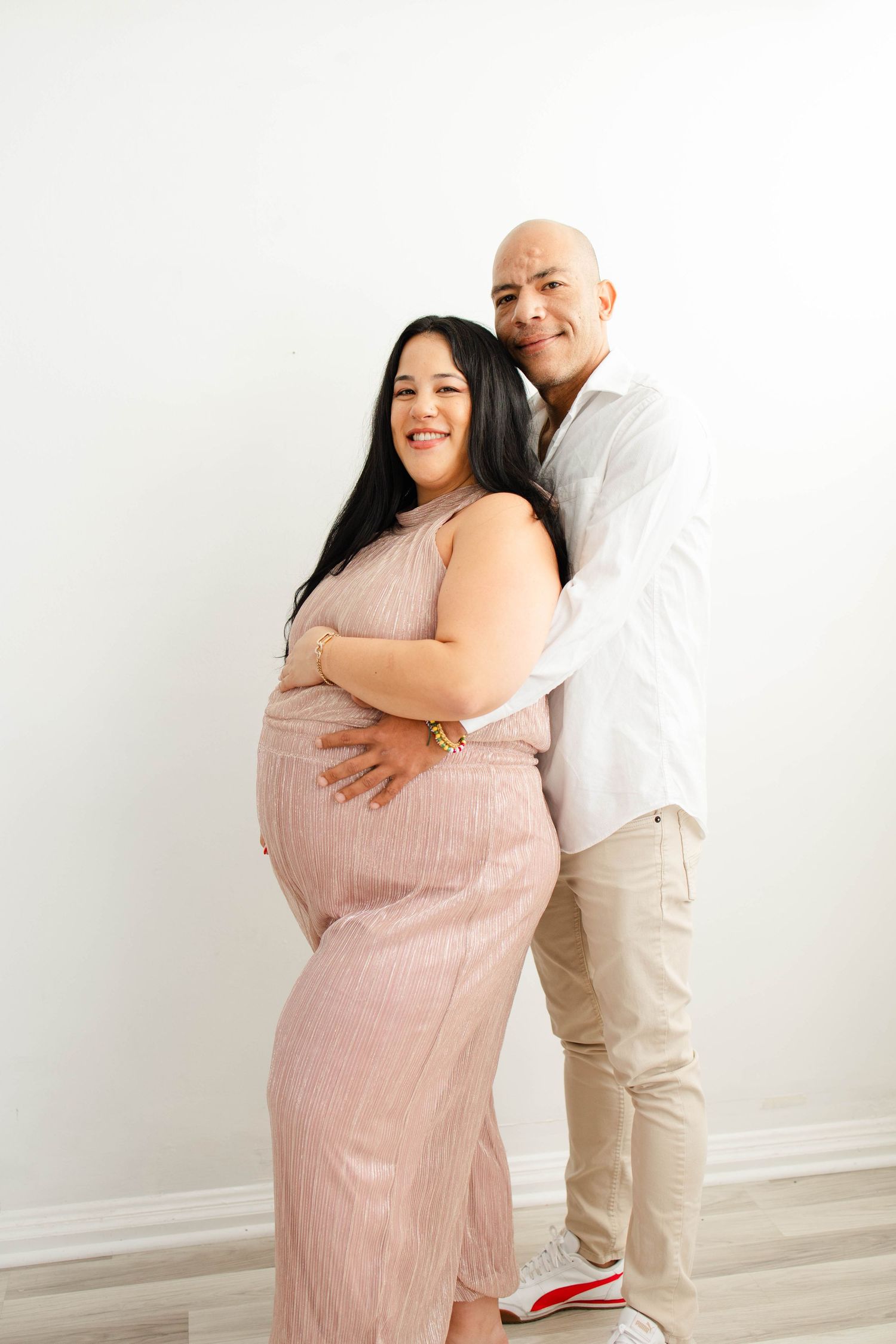 A maternity photoshoot featuring a couple embracing against a white backdrop.
