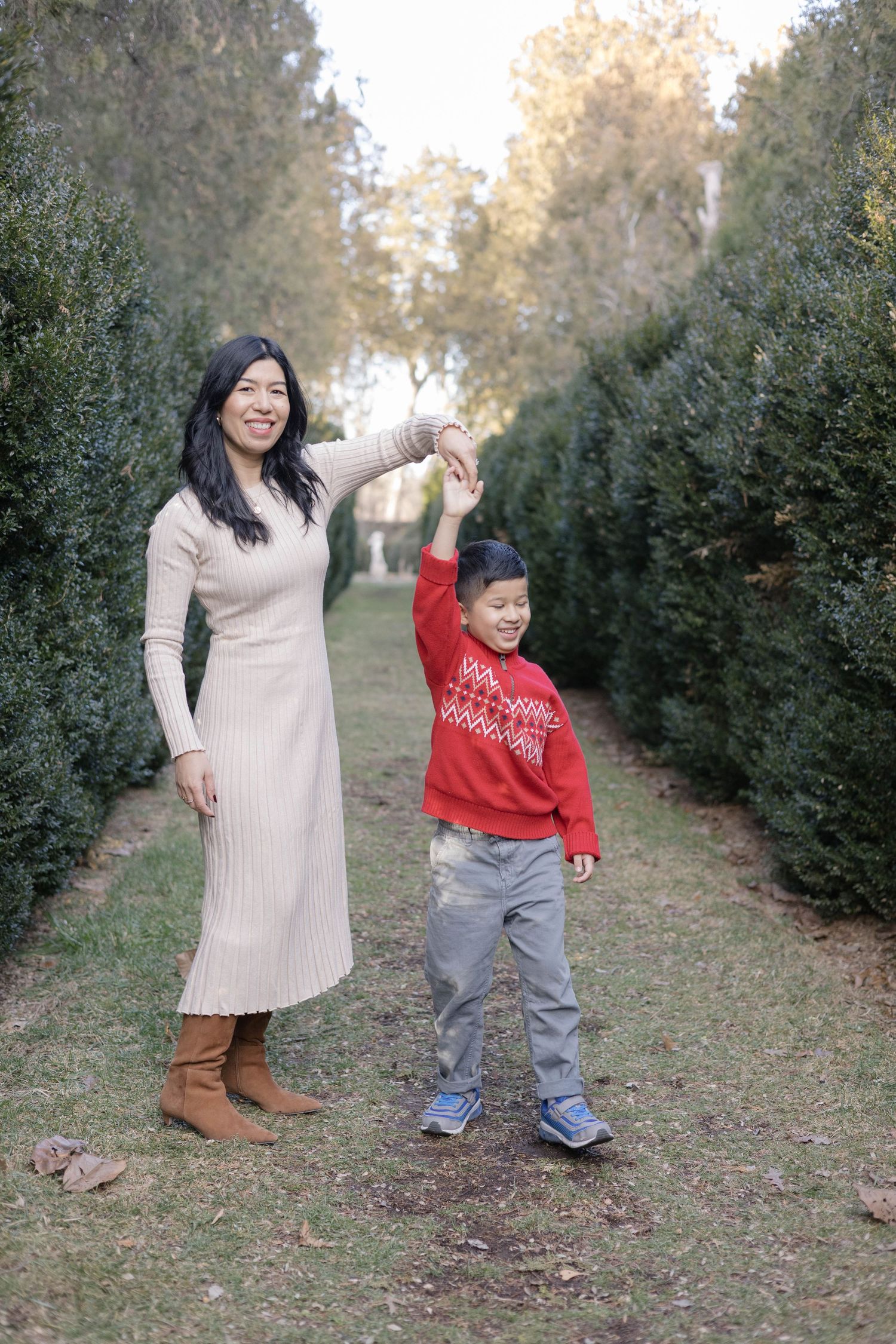 A family shares playful moments between evergreen trees on a fall afternoon.