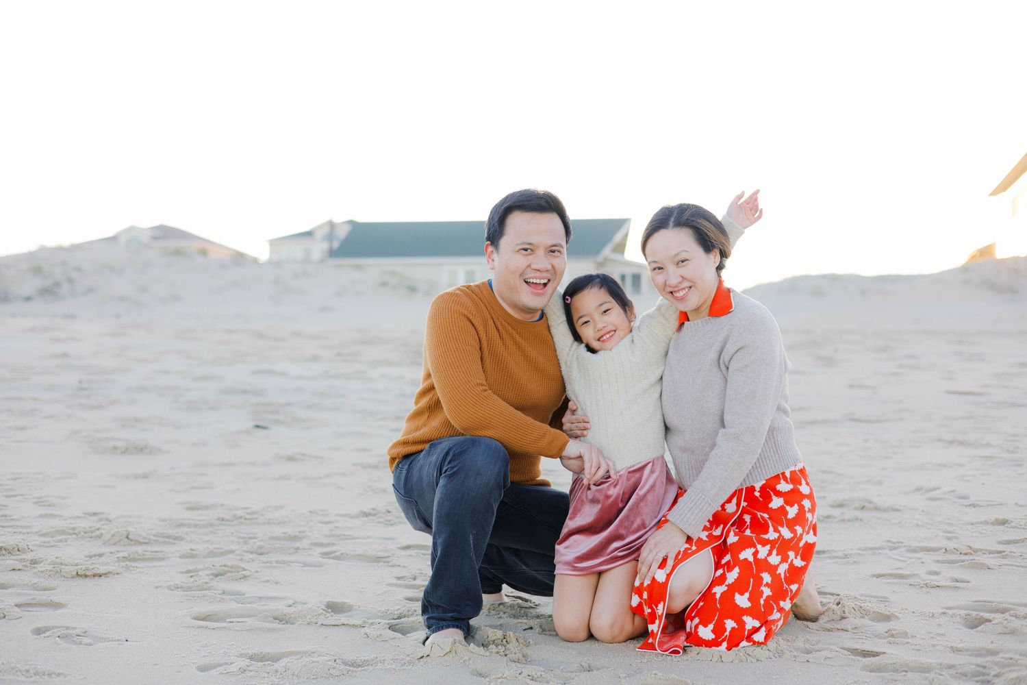 A family of three poses together on a sandy beach during sunset.