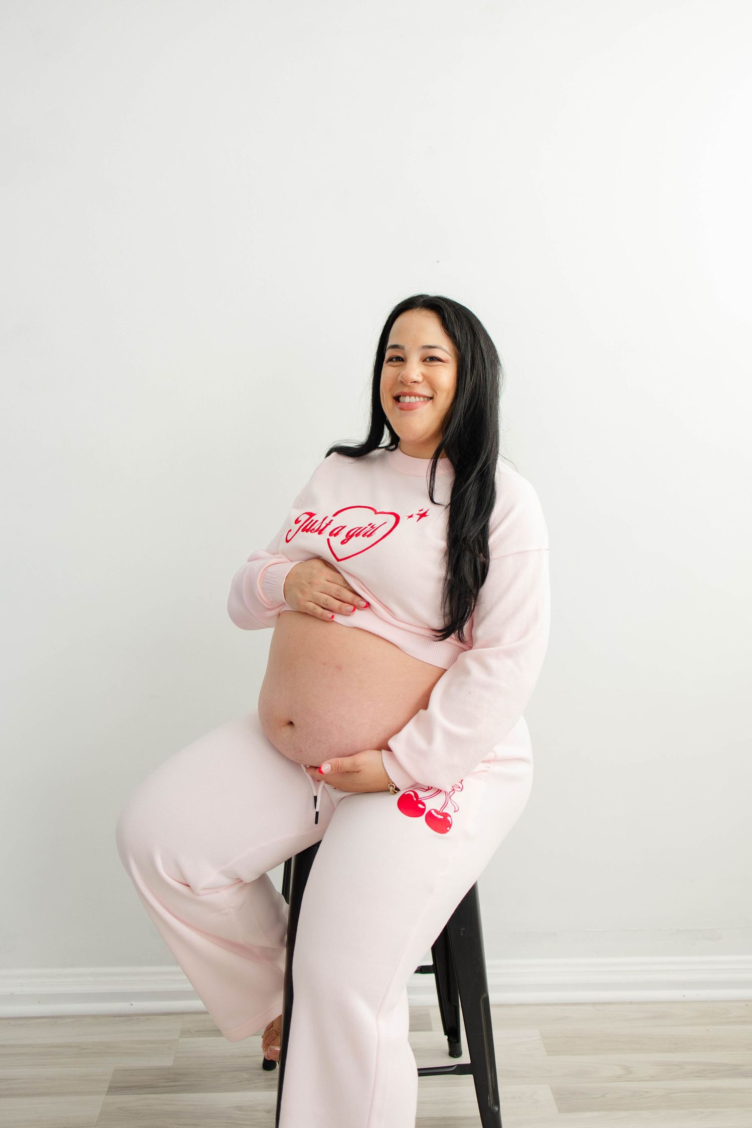 Maternity photos of an expectant mother in pink clothing sitting on a black chair.