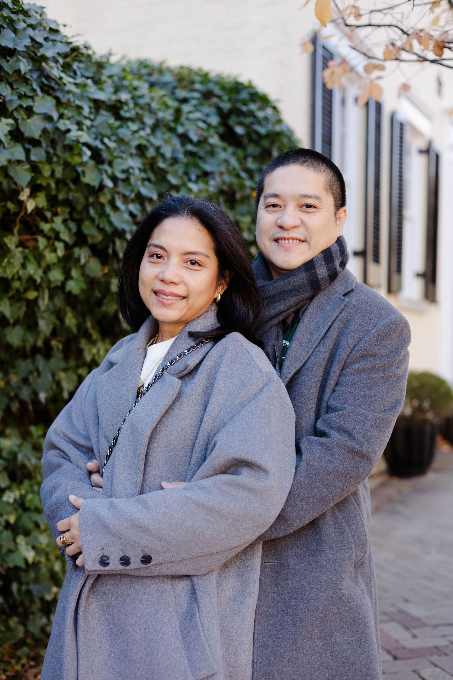 Two people in matching grey coats sharing playful moments outdoors.