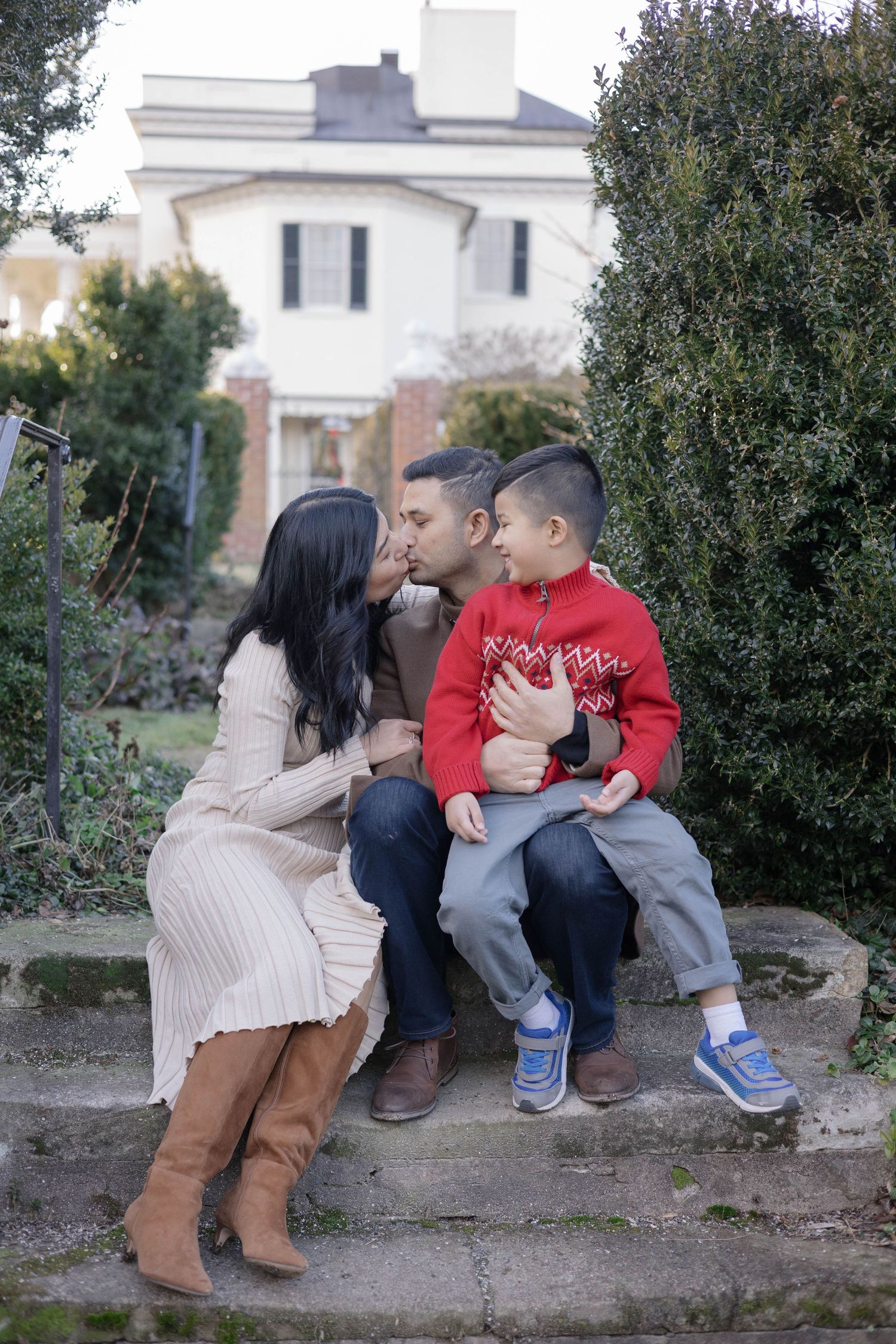 A loving family shares an intimate moment while sitting on a stone wall at a Christmas tree farm.