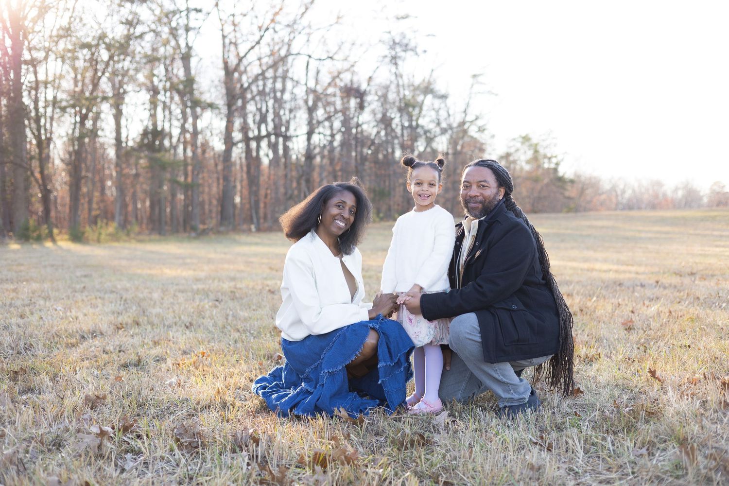 Candid family portrait session in a rustic field with autumn trees in background.