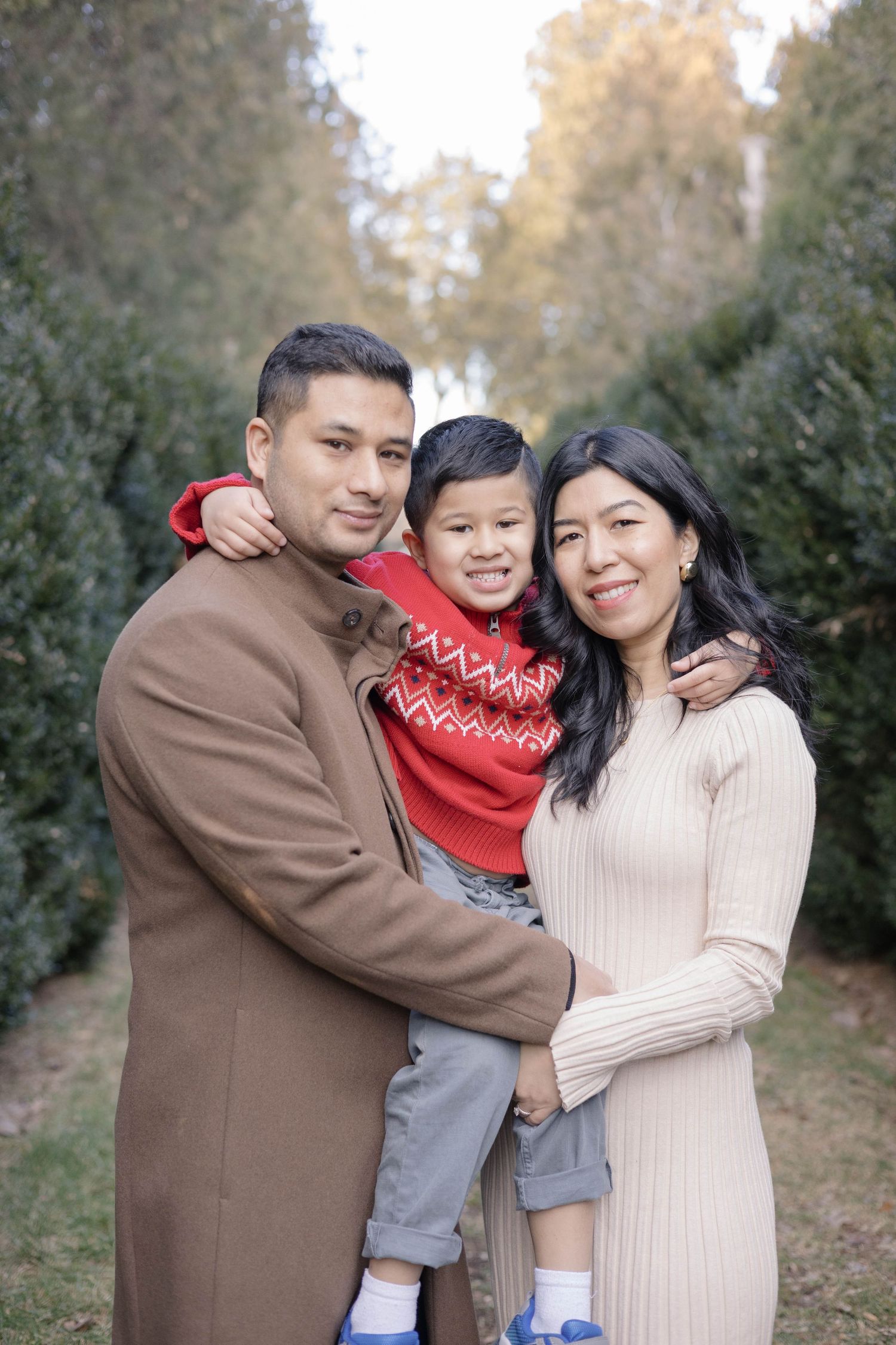 A family poses together in a wooded area wearing coordinated winter outfits of brown and cream.