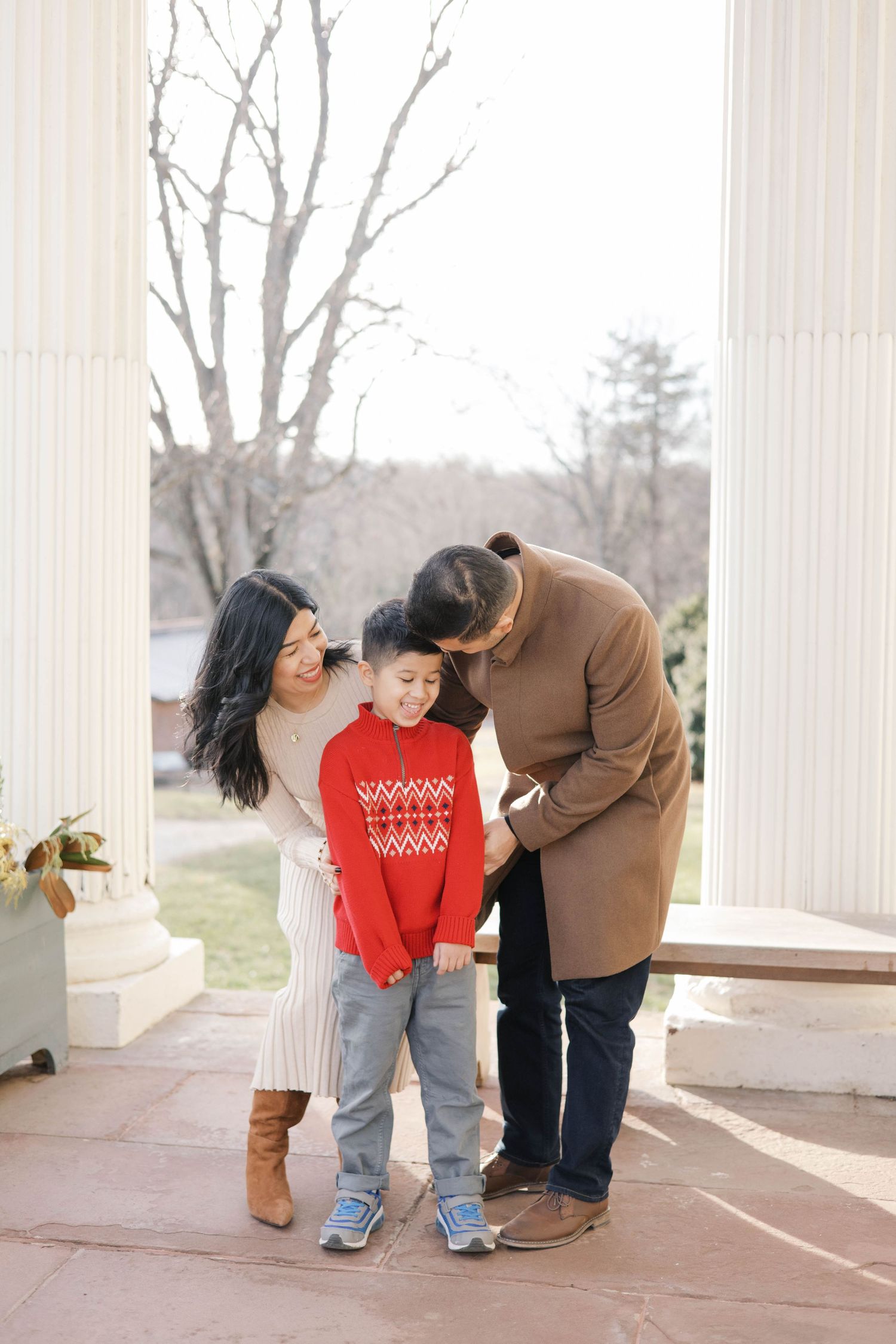 Family sharing intimate moments between white columns on a porch.