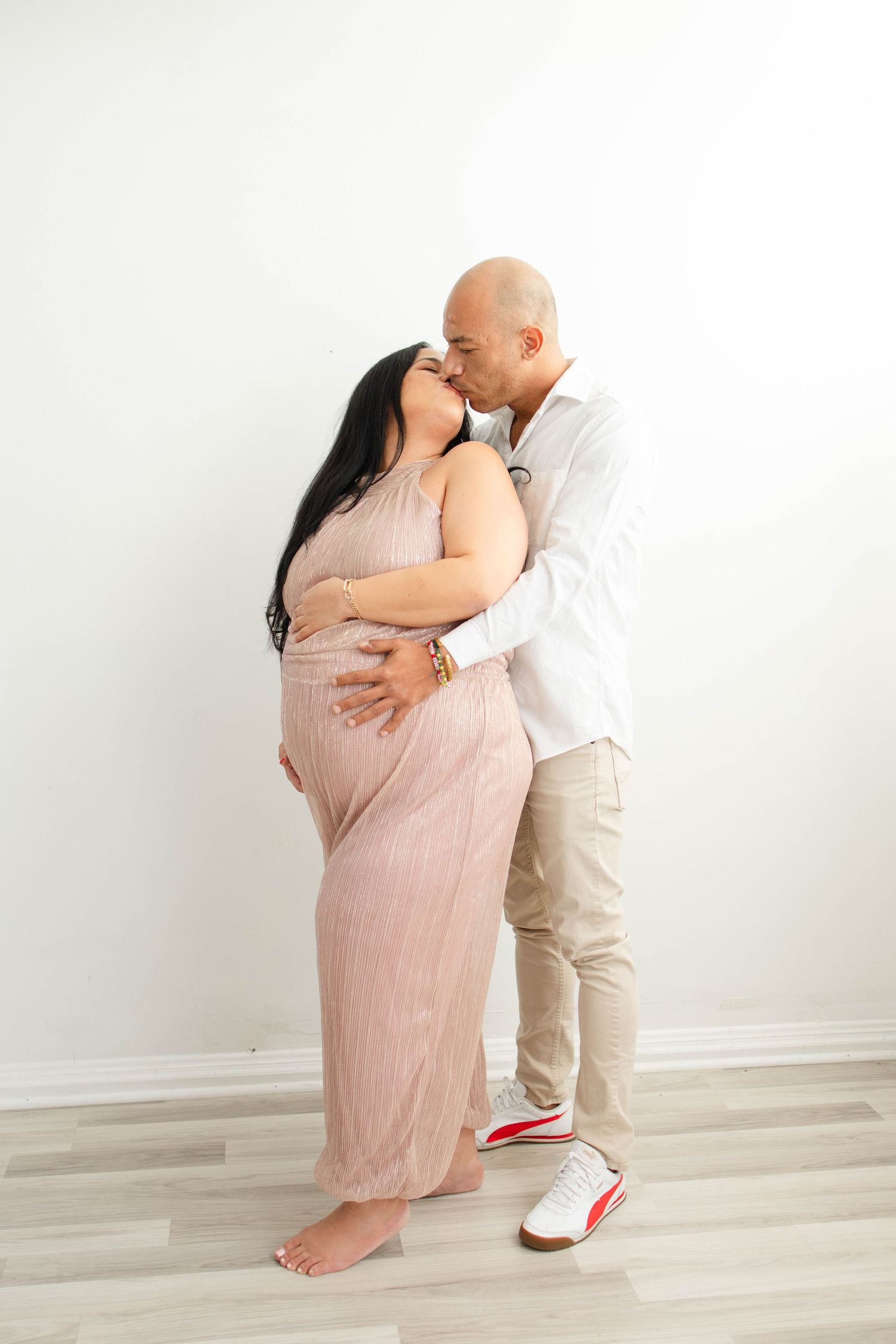 Sweet maternity photoshoot moments captured in a minimalist white studio setting.