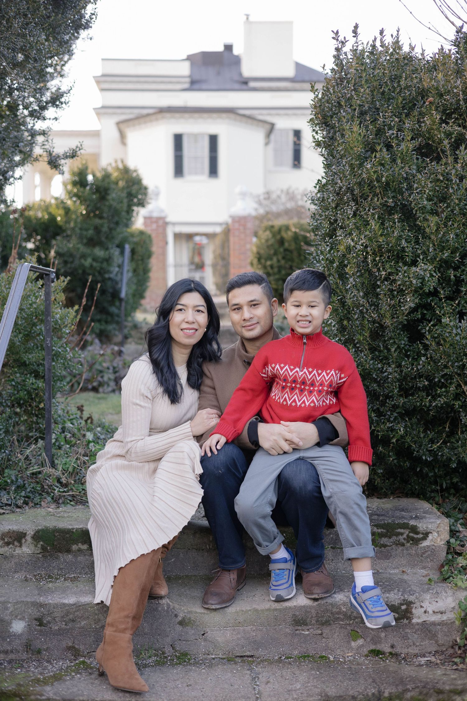 A family sits together on a stone wall with evergreen trees and white buildings in the background.