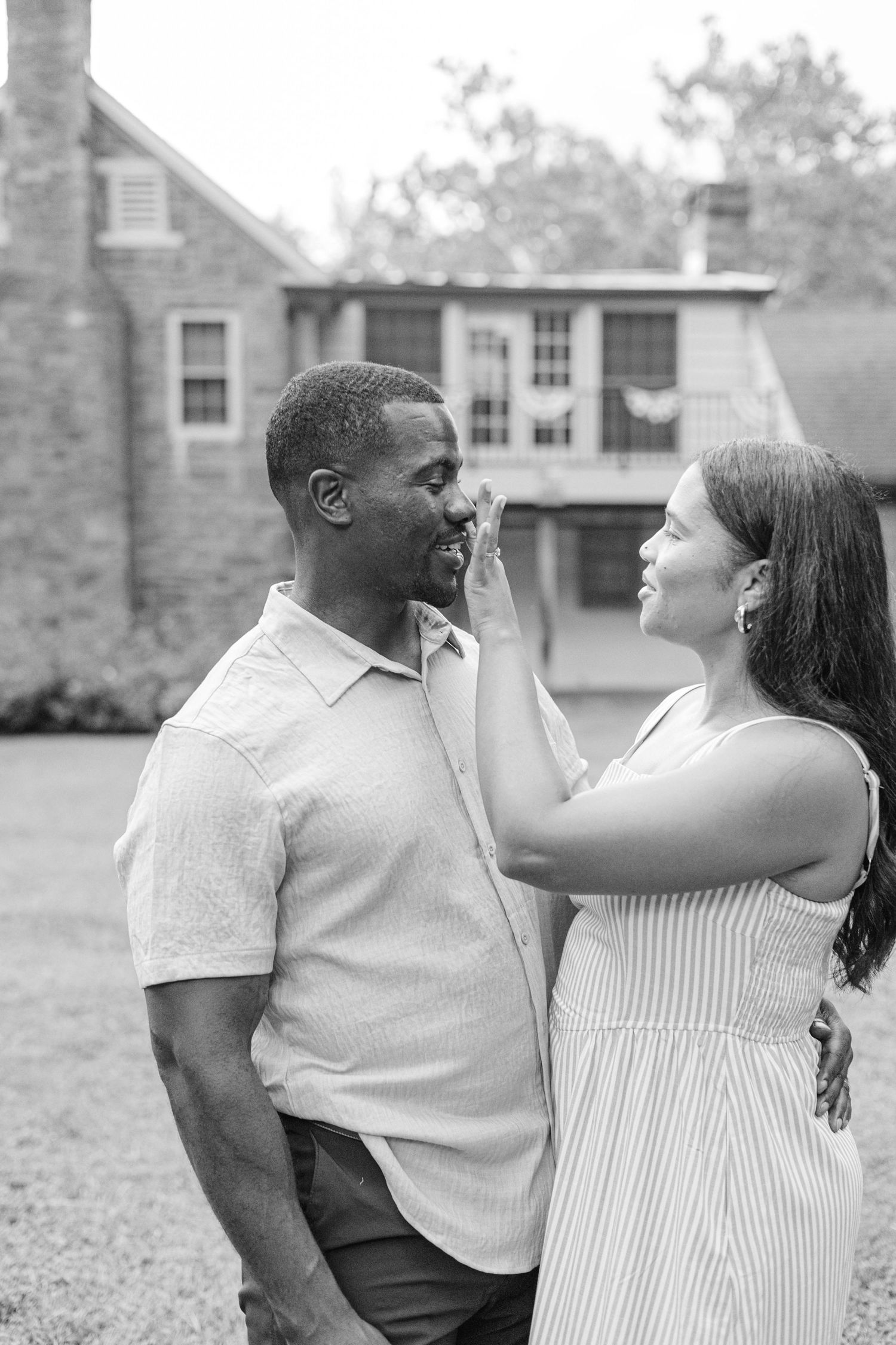 Black and white photo of a couple sharing a tender moment outdoors, woman touching mans face near a historic brick building.