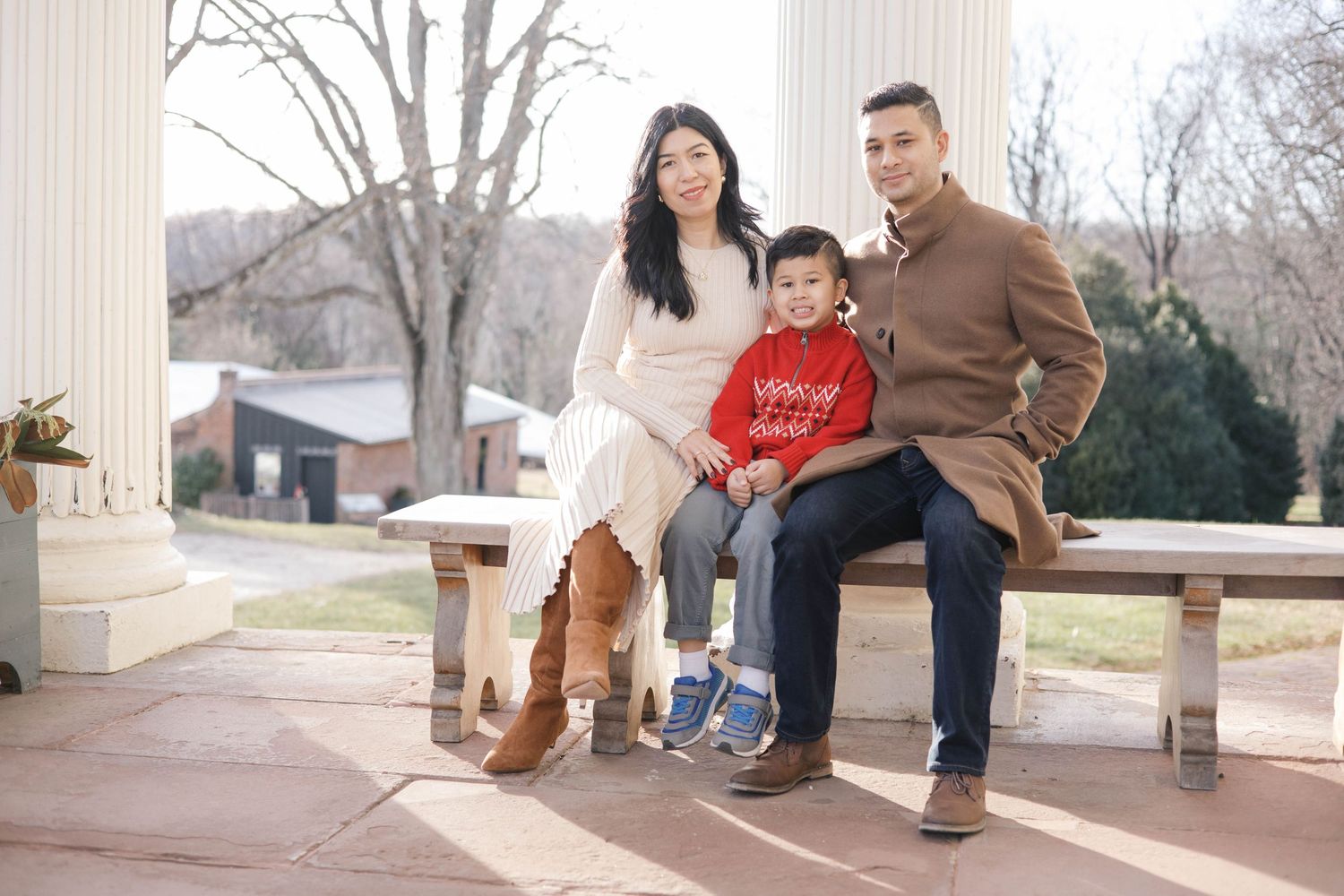 Family poses between classic white columns during outdoor photoshoot.