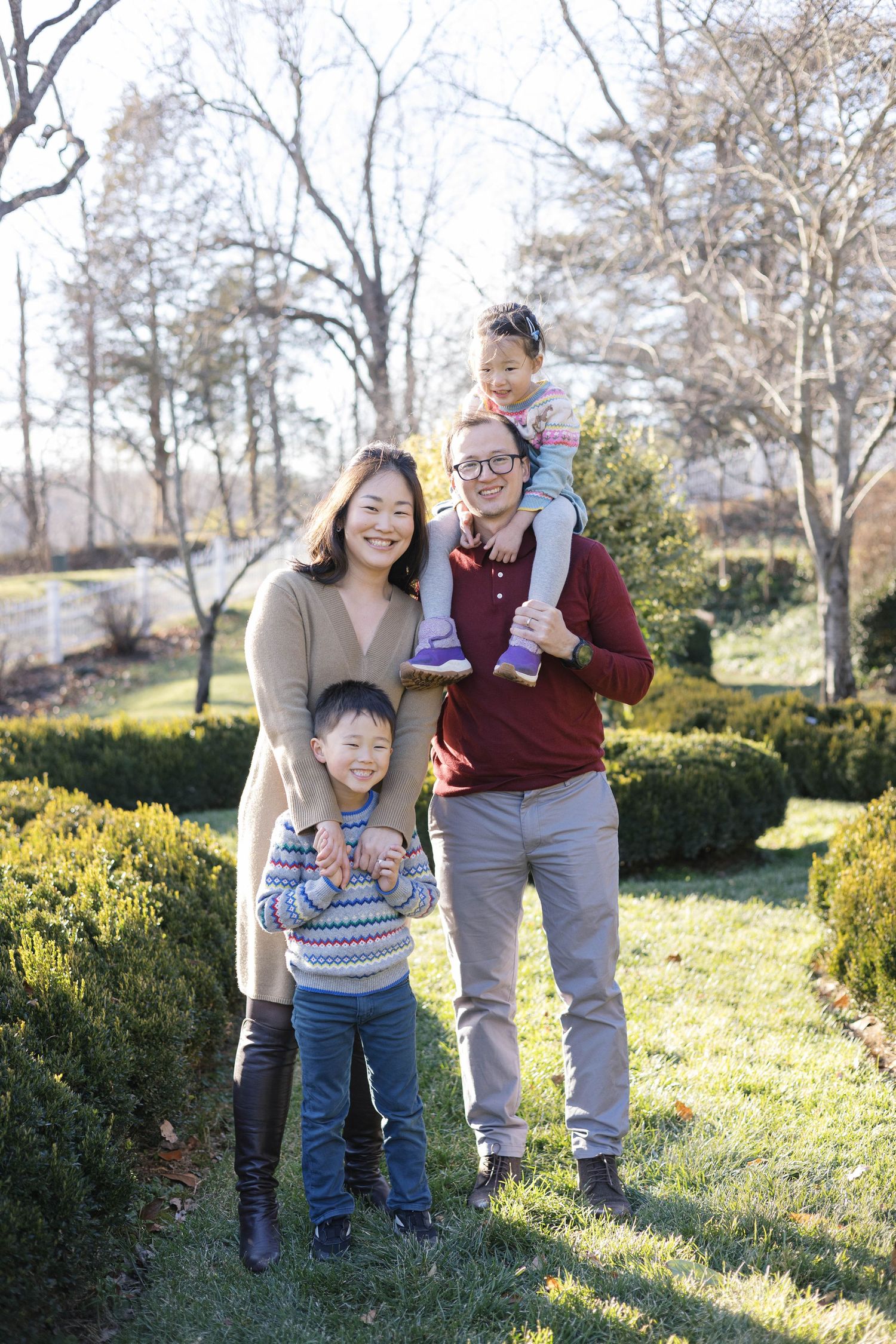 Playful family interactions in a garden setting with green shrubs and winter trees.