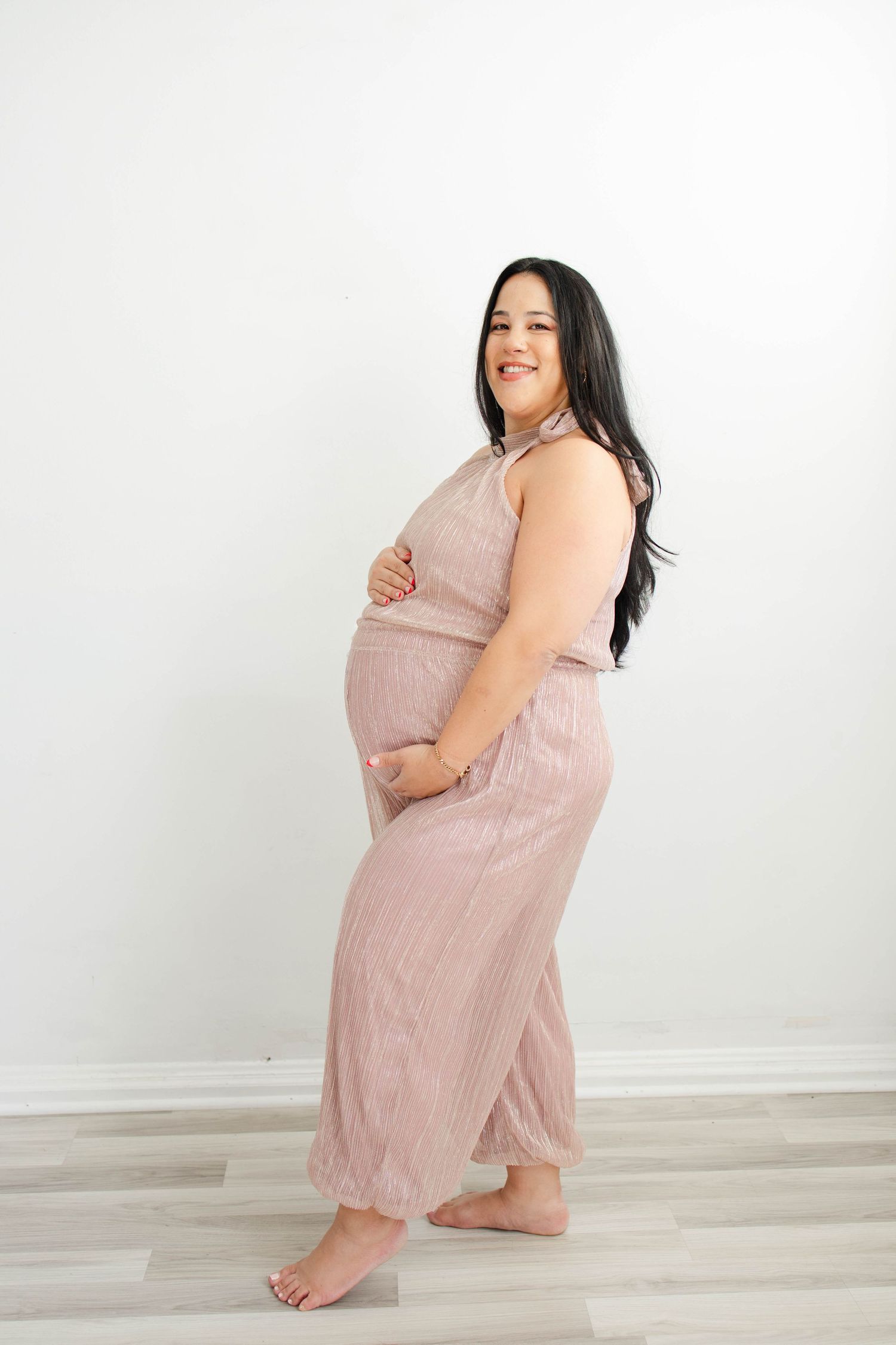 Expectant mother in pink outfit poses joyfully during studio maternity session.
