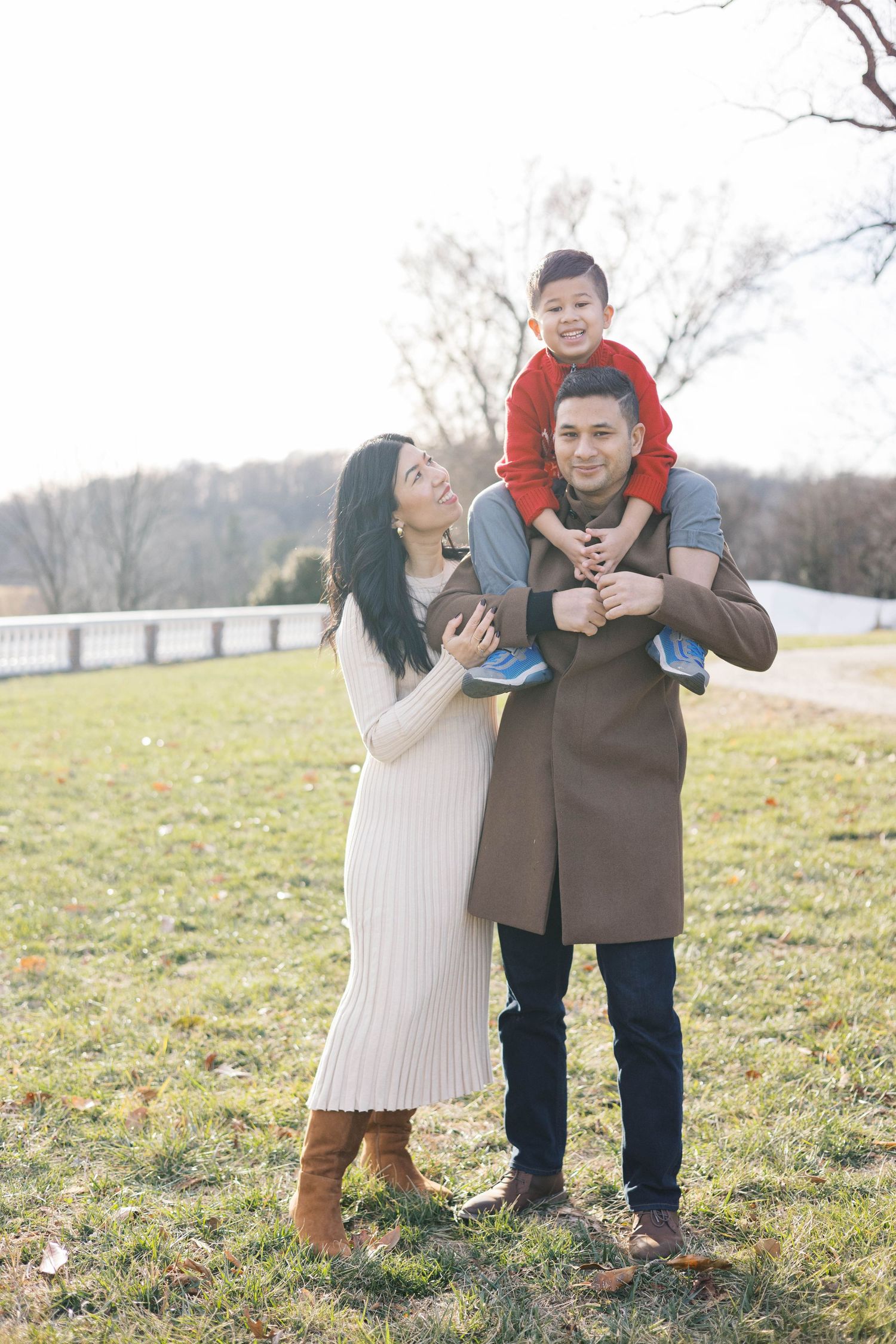 A tender family moment shared on a grassy hill with white fencing in the background.