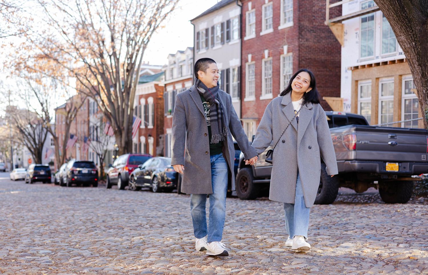 A couple holding hands while strolling down a tree-lined urban street.