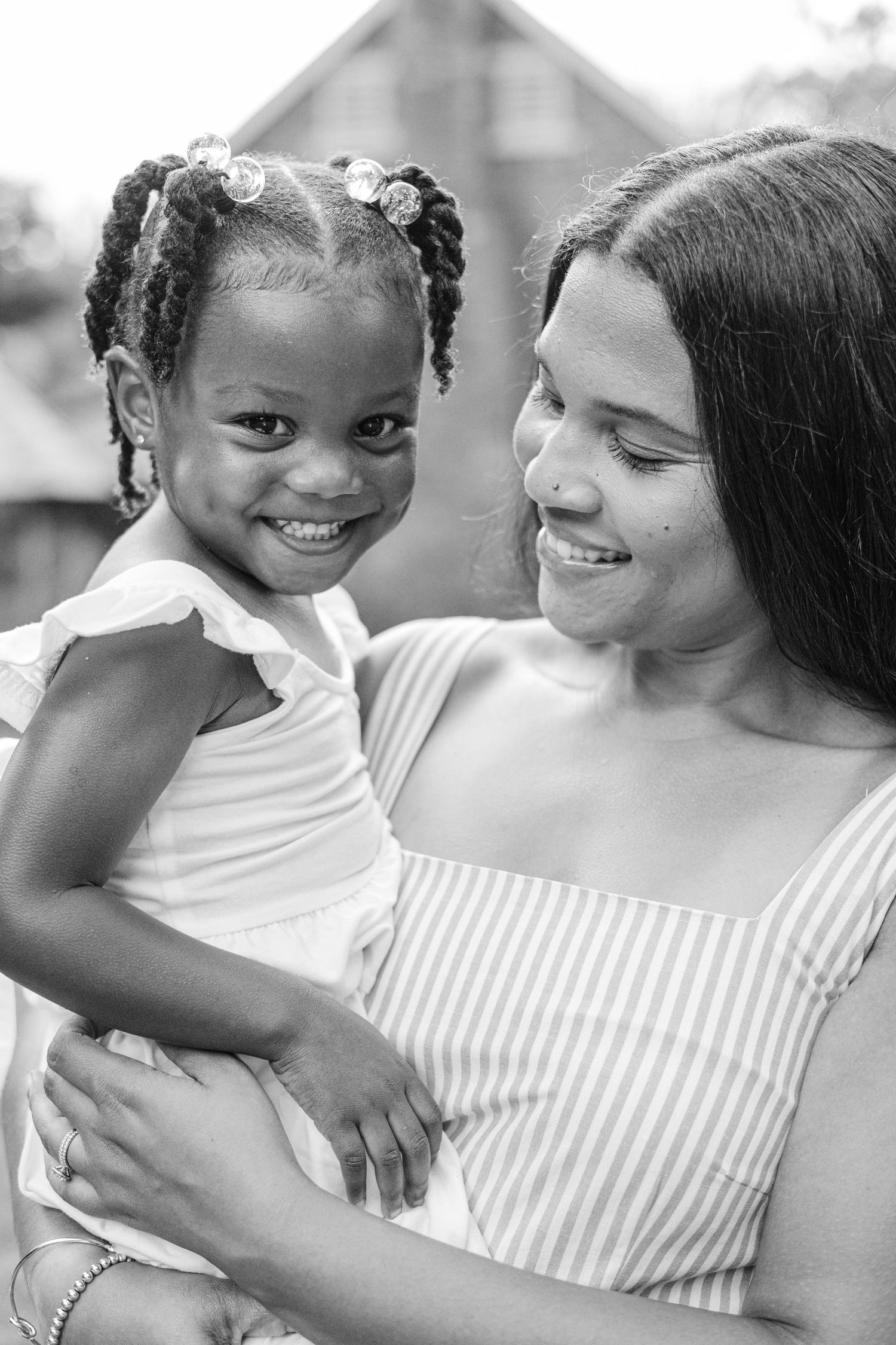 Black and white portrait of a smiling young girl being held by a woman in a striped dress outdoors.