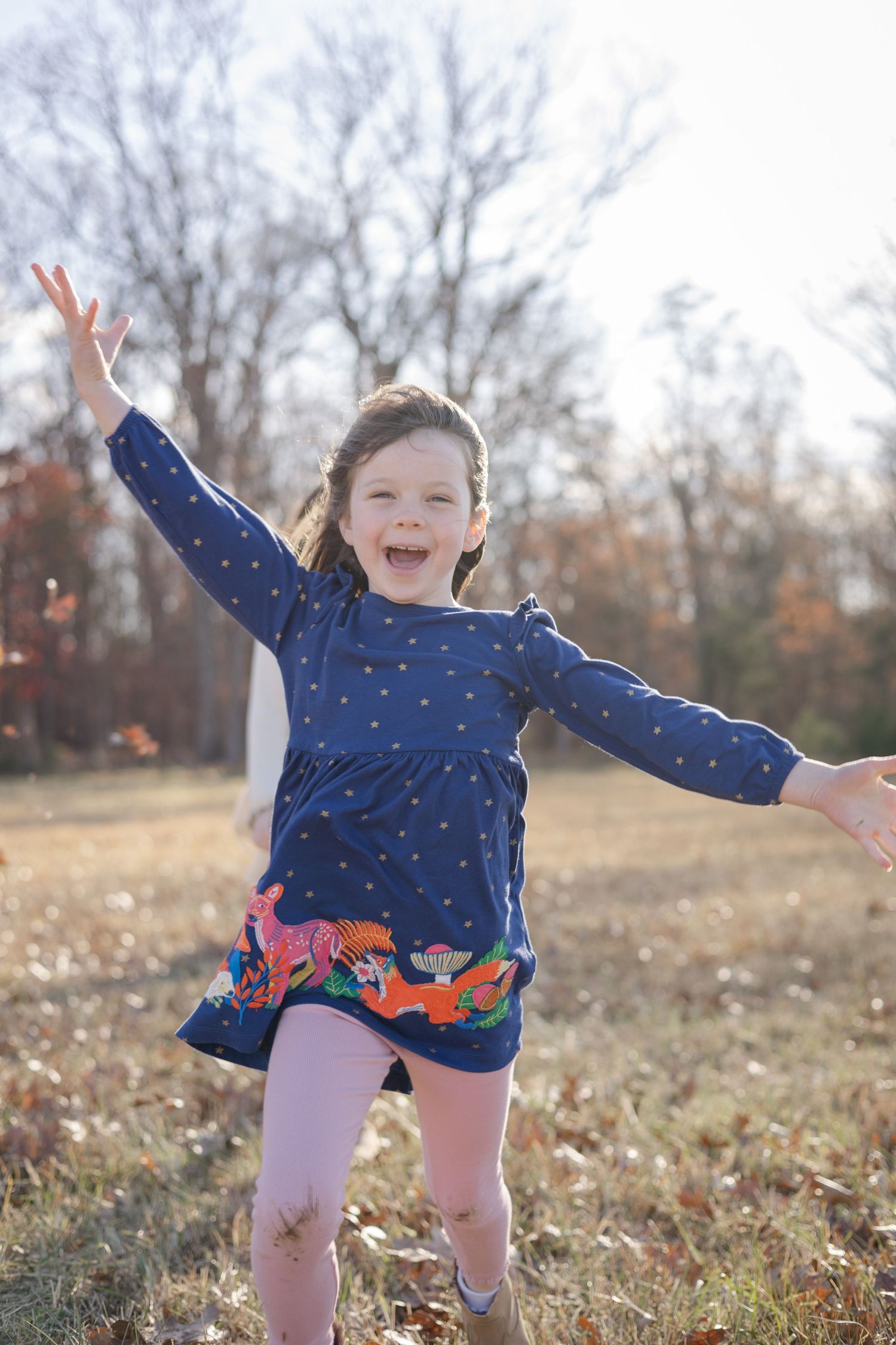 Child in blue polka dot dress jumping joyfully in autumn field.