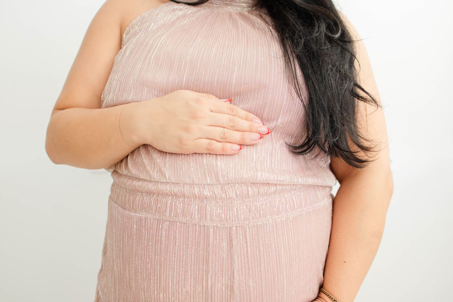 Pregnant woman in pink dress cradling her baby bump against white background.