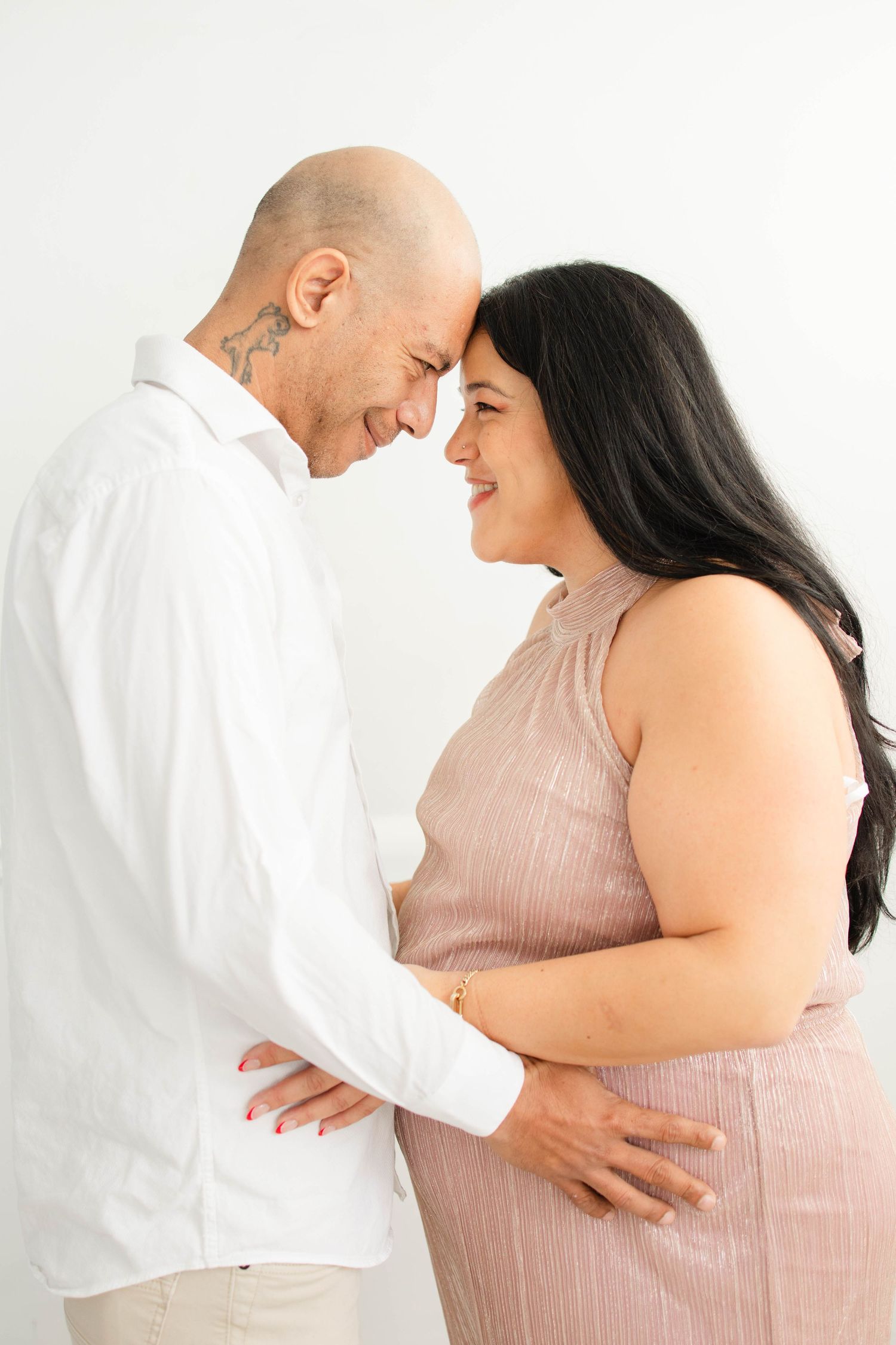 Loving couple shares intimate moment during pregnancy photoshoot in studio setting.