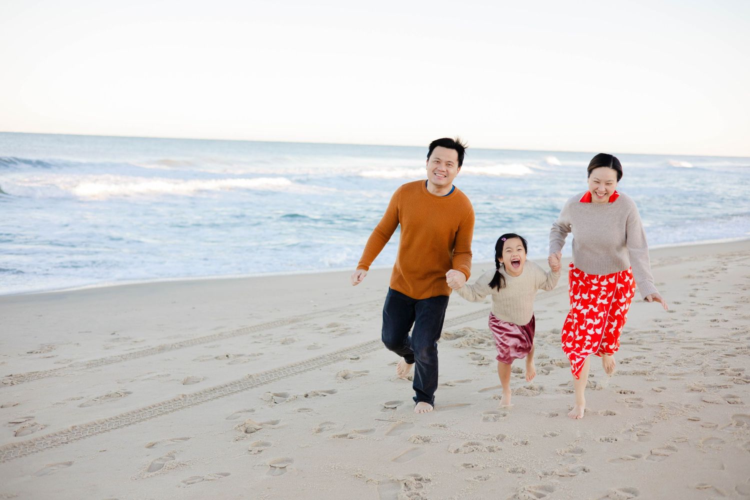 Family members running and playing together along the ocean shoreline.