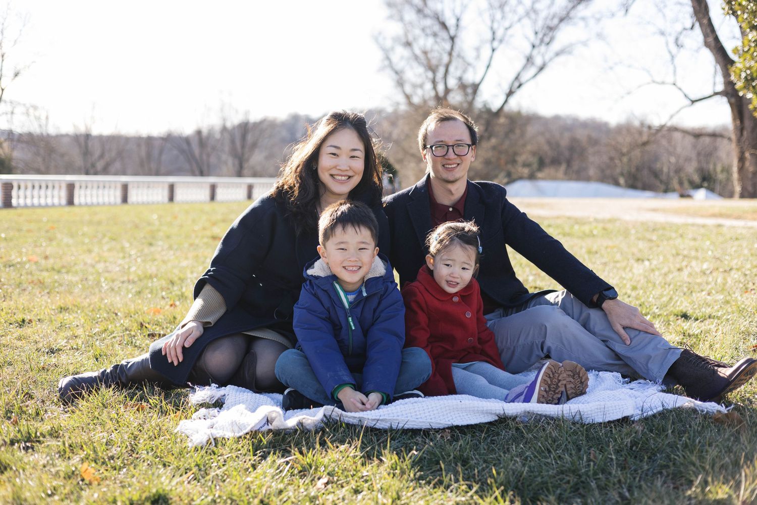 Family lying together on a blanket in a sunny field during an outdoor photo session.