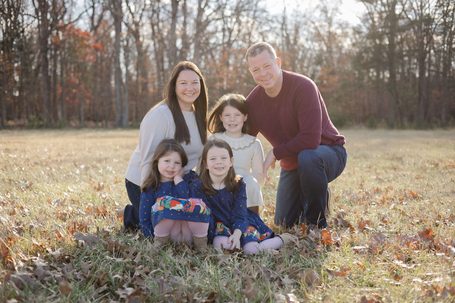Family sitting together in a field with autumn foliage and trees.
