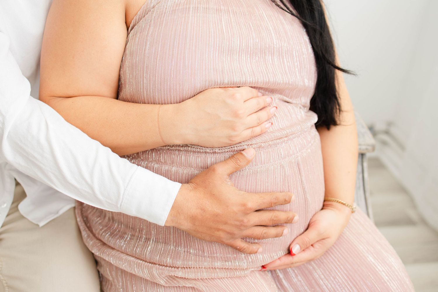 Close up of hands cradling baby bump in pink textured dress.