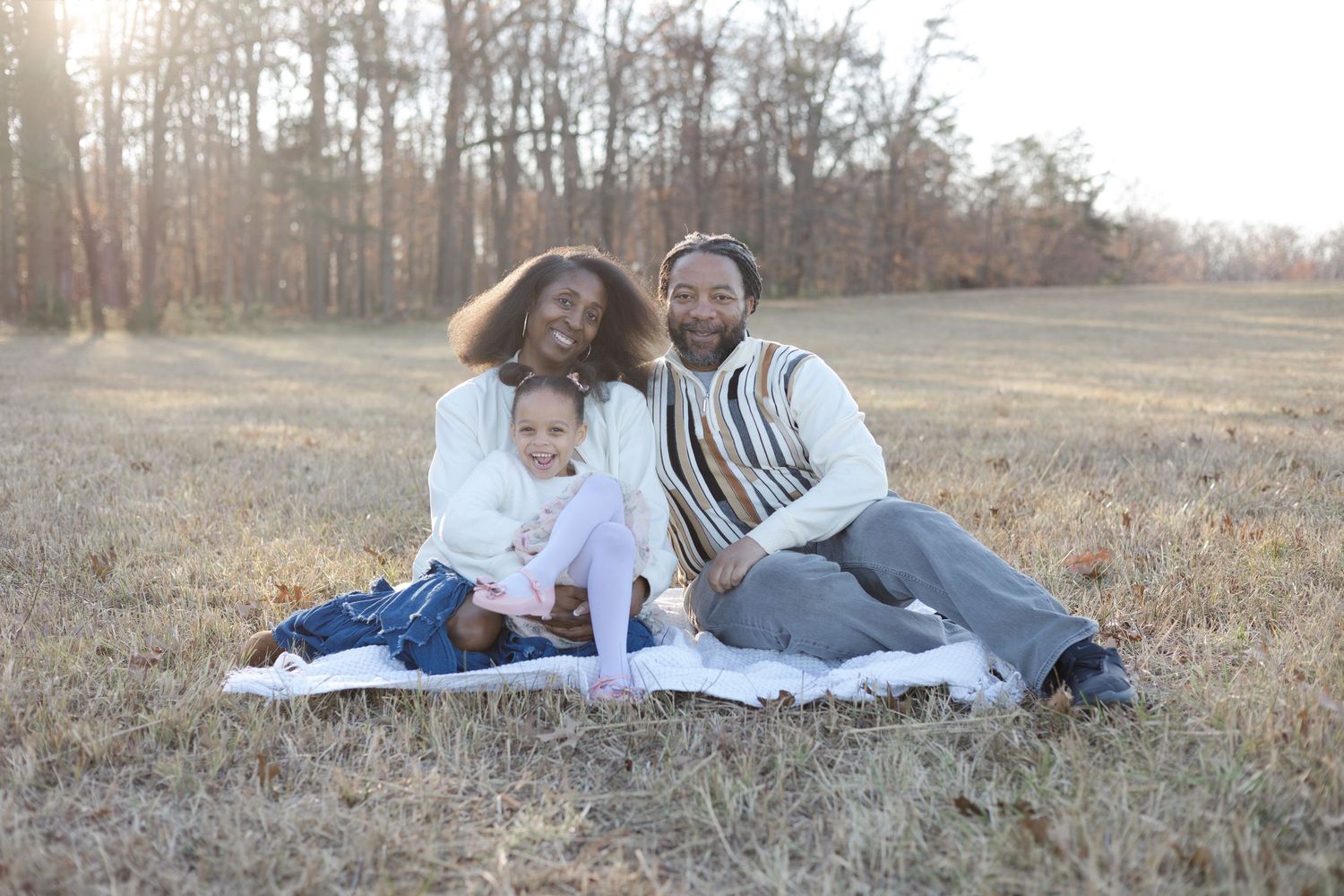 Family relaxing on white blanket during outdoor photo session at sunset.