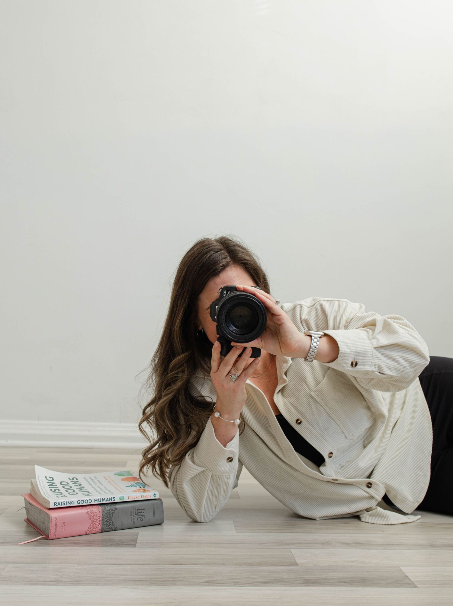 Photographer in white button down shirt lying on floor with camera and books in minimalist setting.