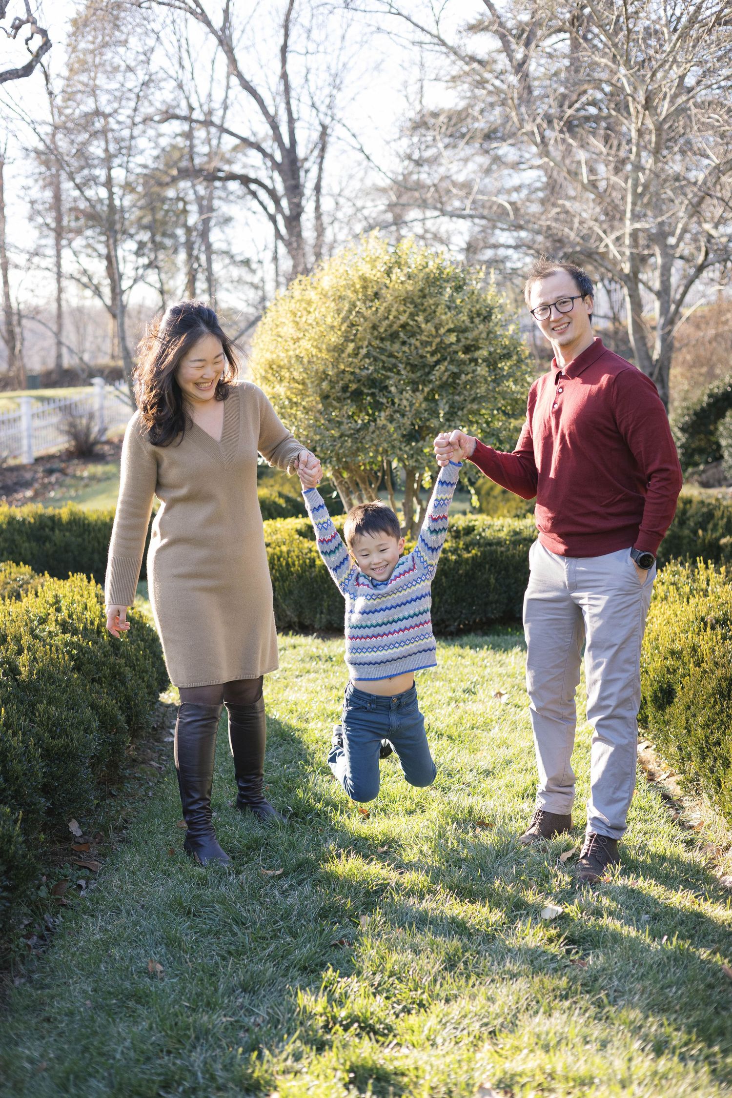 Family having fun and jumping together on grassy hill with shrubs in background.