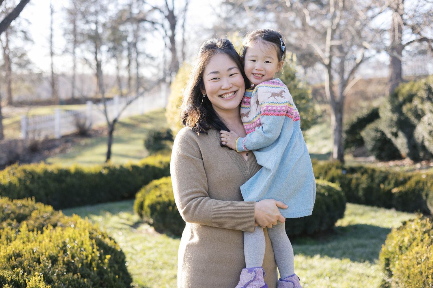 Loving family embraces while standing in a sunlit garden with evergreen landscaping.