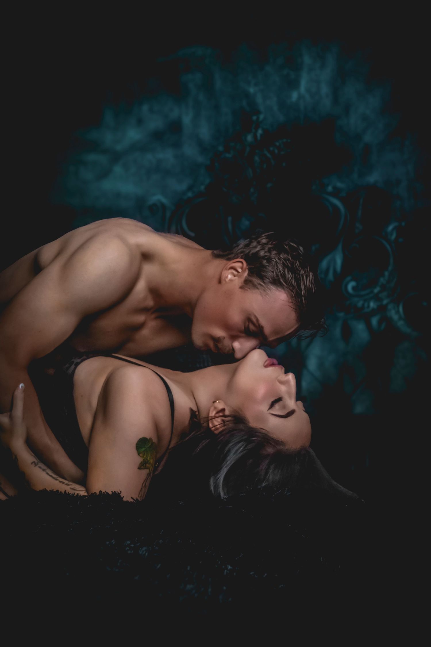 Intimate couple boudoir photography with moody blue lighting and dark background.